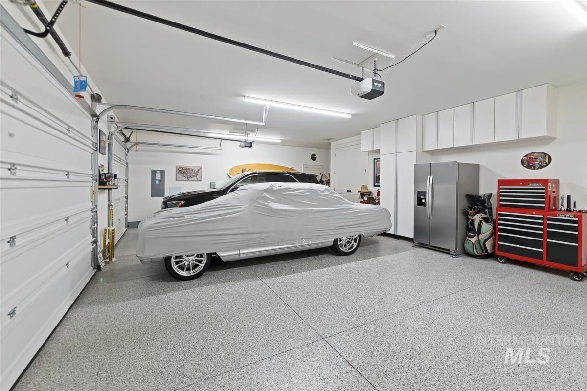 Garage with stainless steel fridge with ice dispenser, electric panel, and a garage door opener