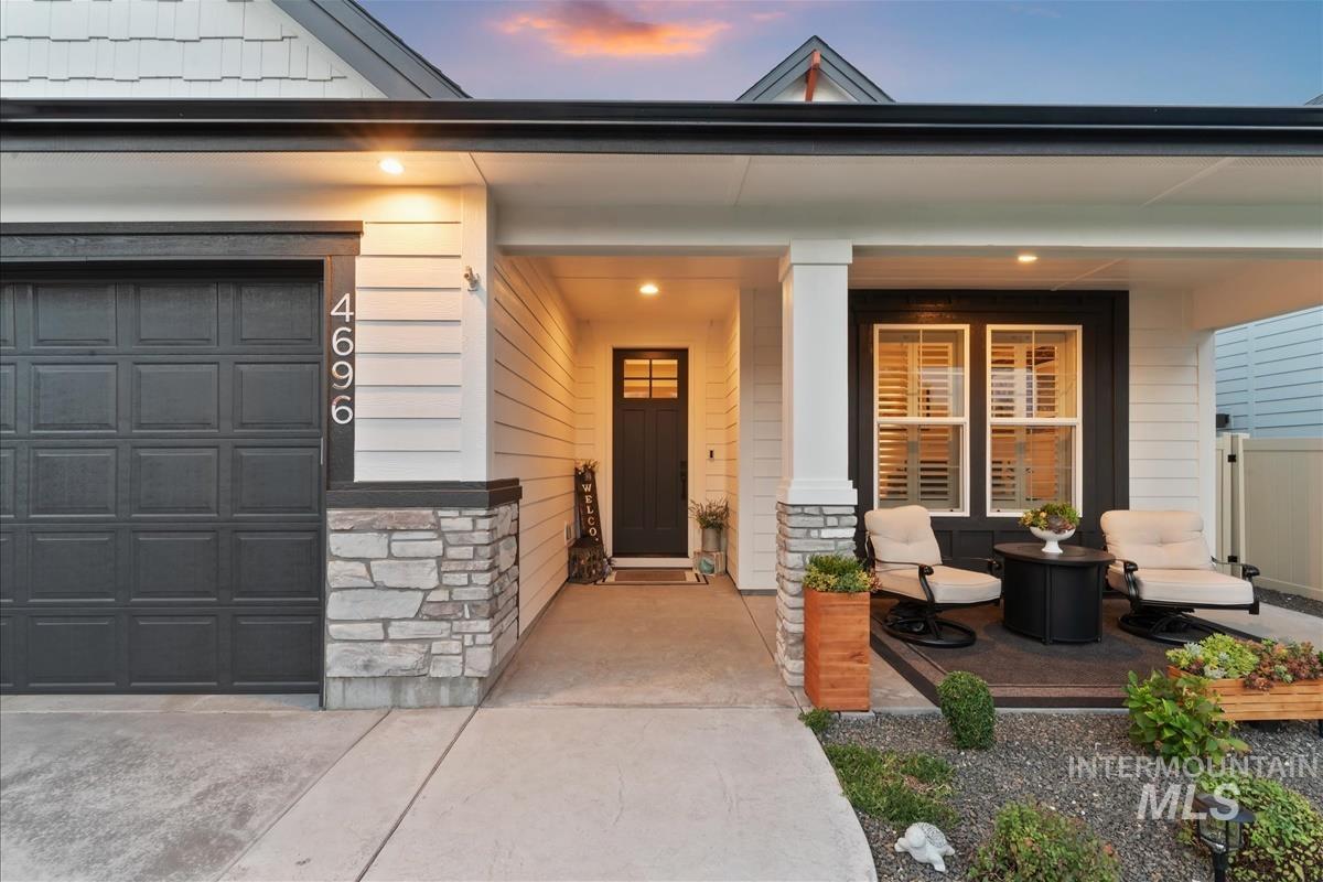 Exterior entry at dusk with a porch, stone siding, and a garage
