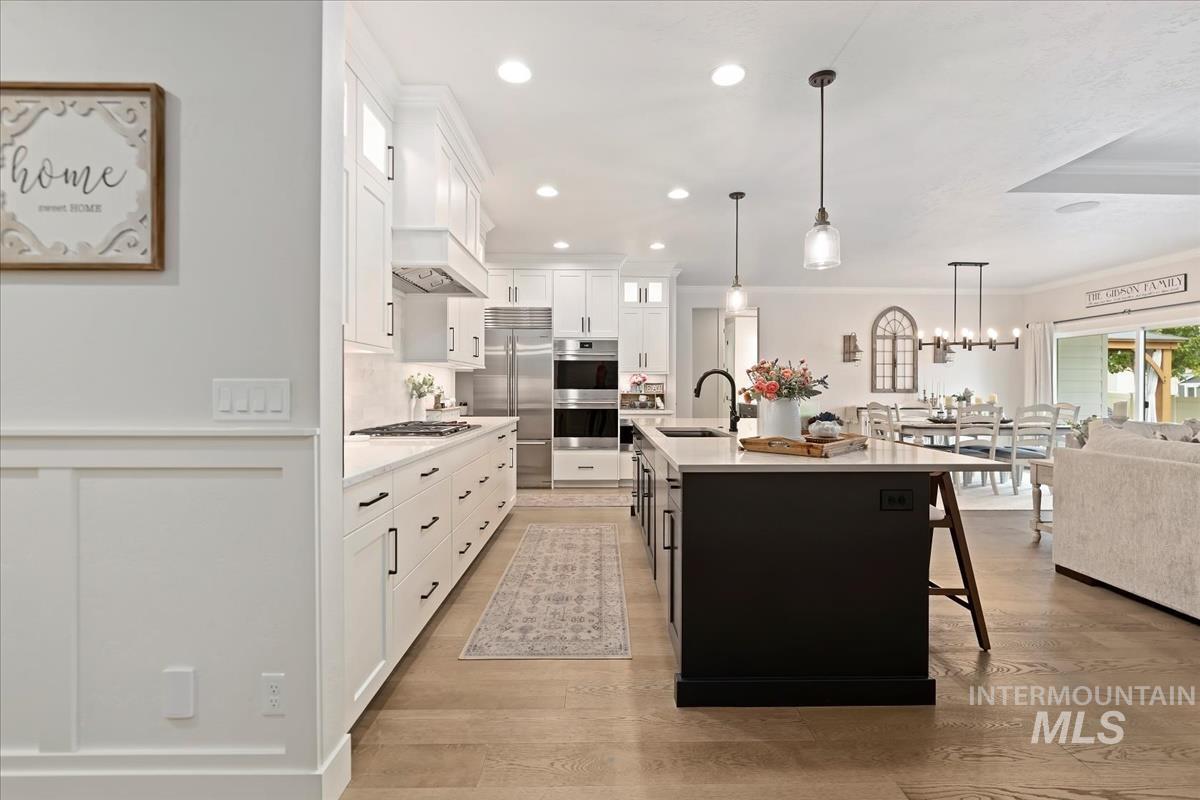 Kitchen with open floor plan, pendant lighting, recessed lighting, glass insert cabinets, and an island with sink