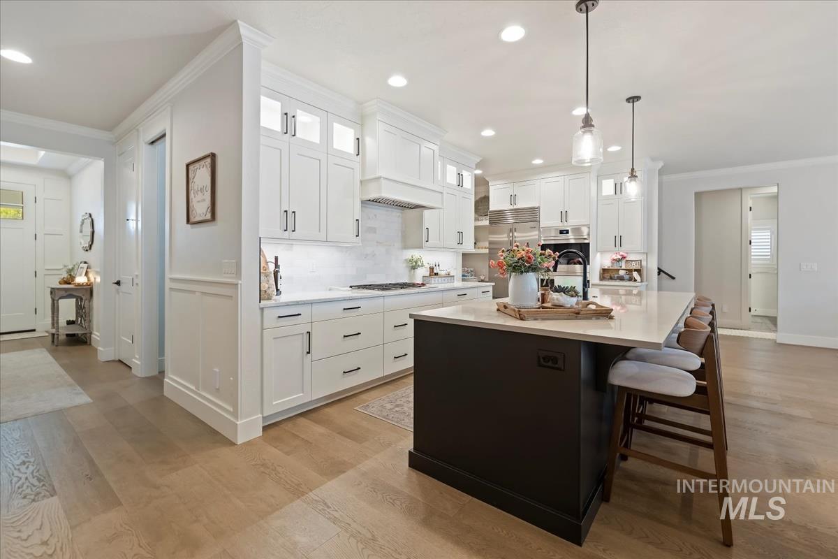 Kitchen with glass insert cabinets, crown molding, white cabinets, tasteful backsplash, and a kitchen island with sink