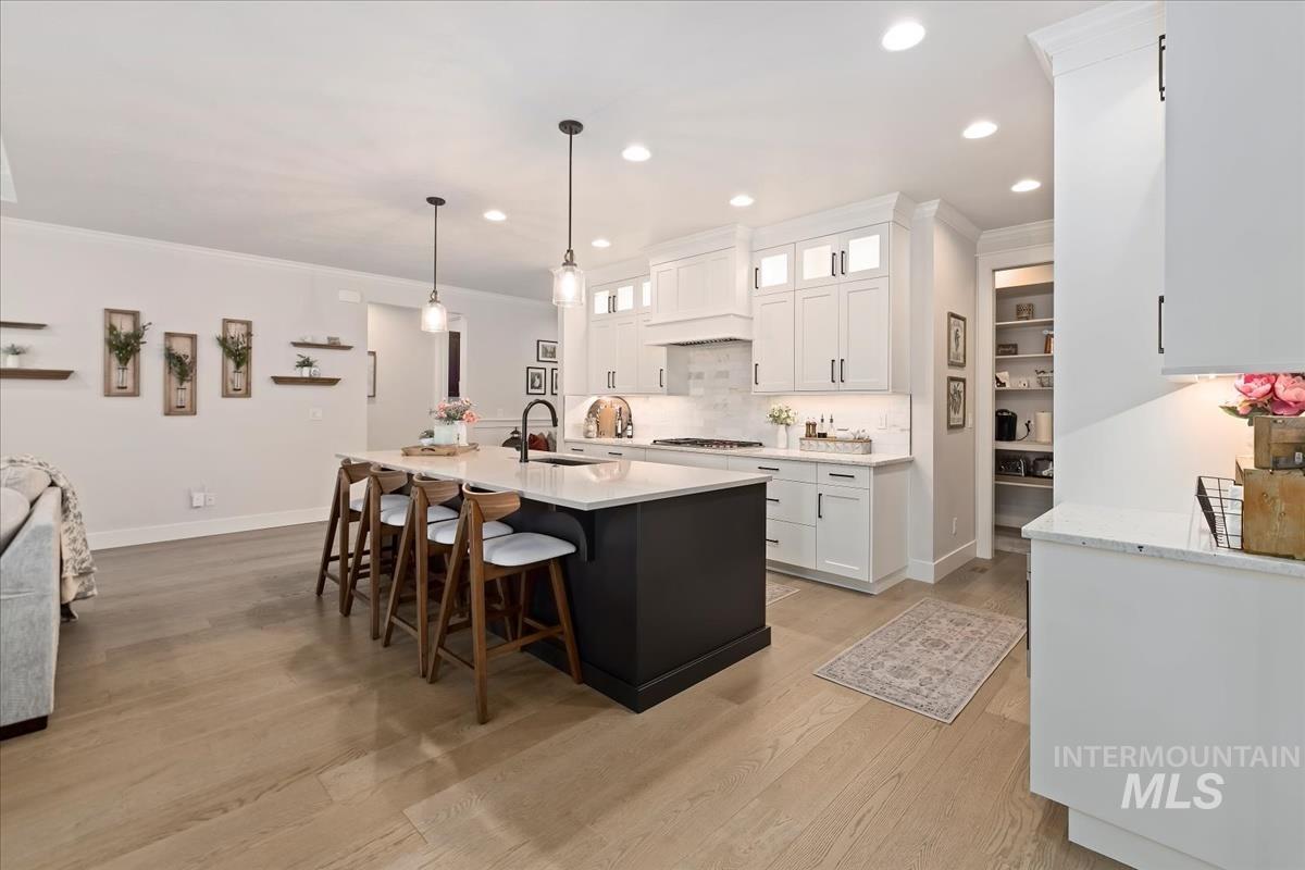 Kitchen featuring crown molding, white cabinetry, pendant lighting, a kitchen bar, and glass insert cabinets