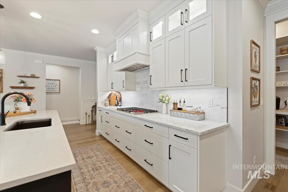 Kitchen featuring hanging light fixtures, ornamental molding, light wood-type flooring, light stone counters, and white cabinets