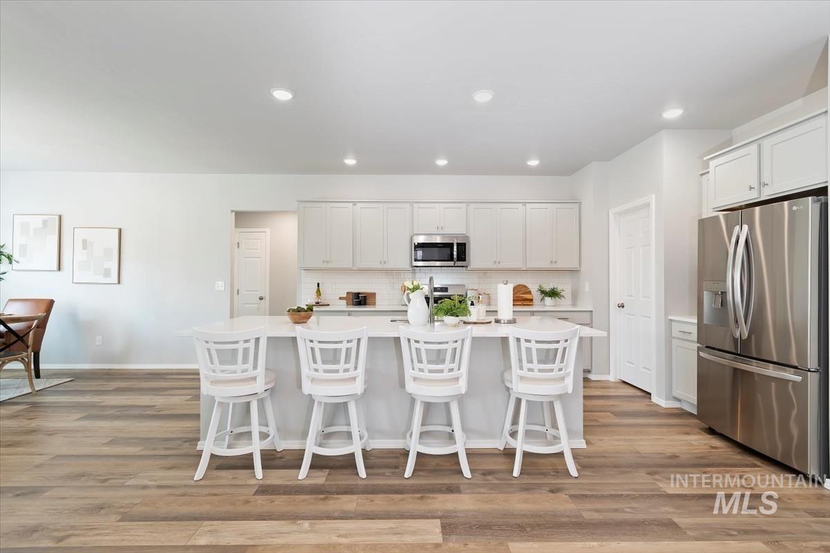 Kitchen with appliances with stainless steel finishes, a kitchen island with sink, a kitchen bar, light wood-style flooring, and decorative backsplash