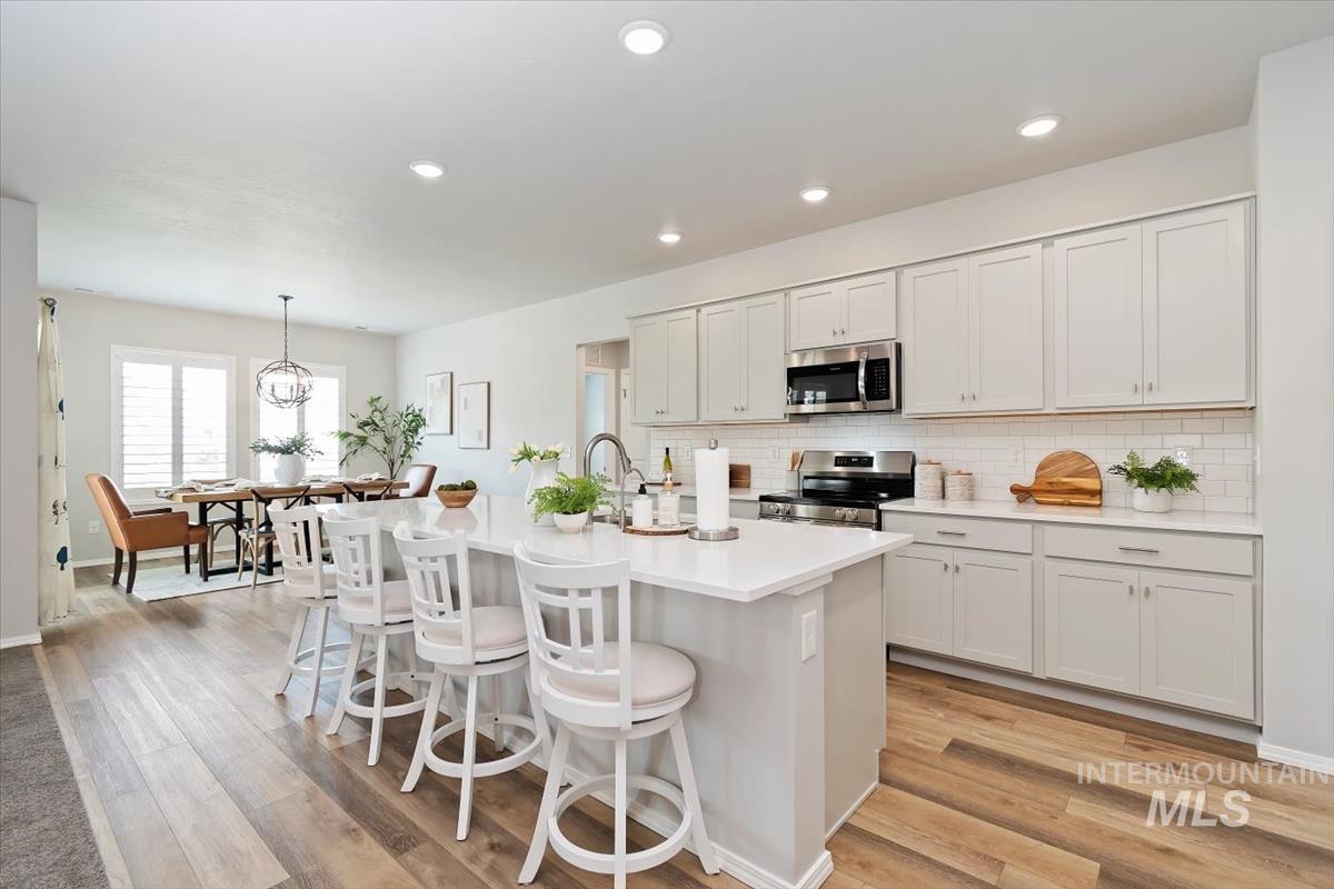 Kitchen featuring a breakfast bar, stainless steel appliances, a kitchen island with sink, hanging light fixtures, and white cabinets