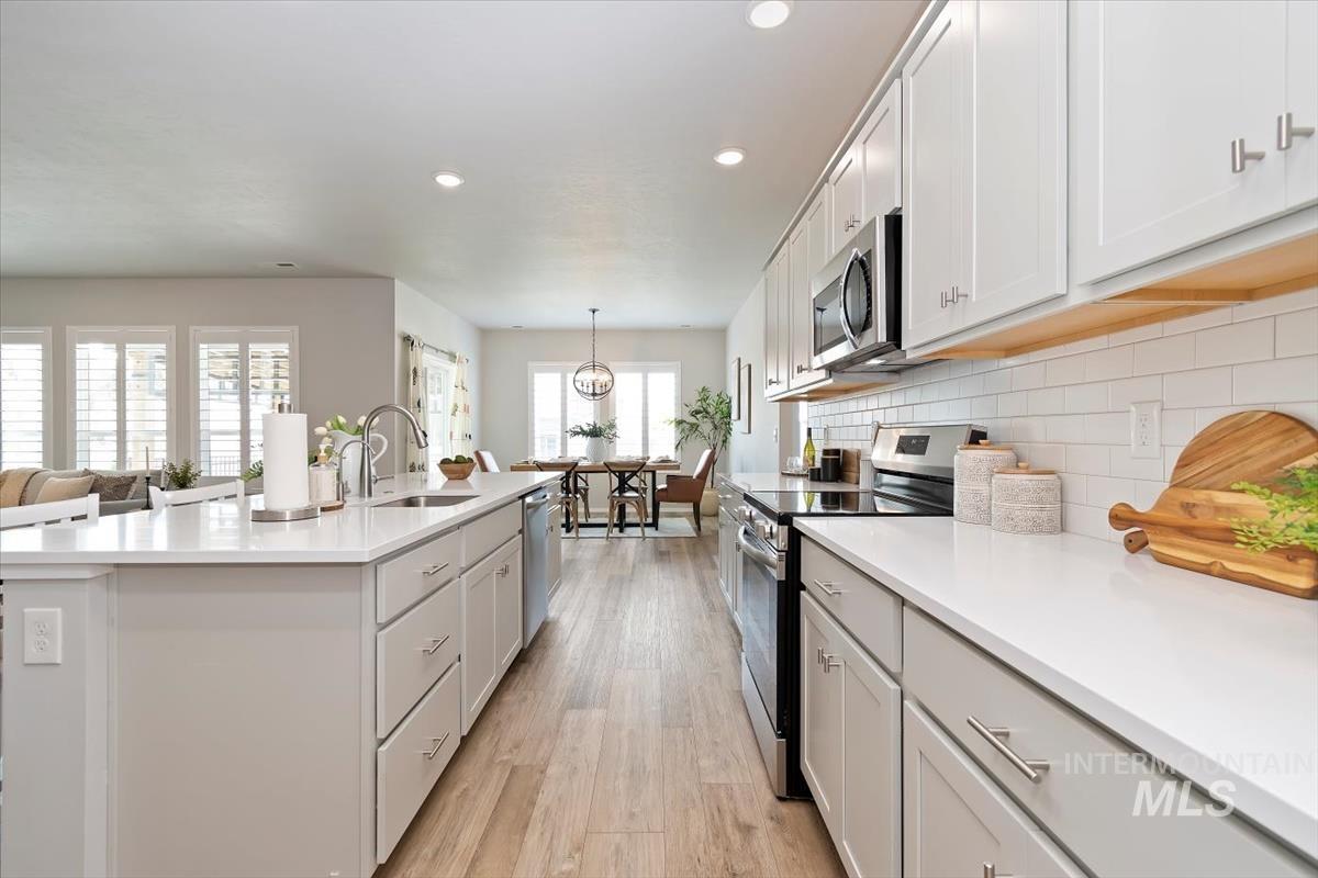 Kitchen featuring stainless steel appliances, light wood-style flooring, decorative backsplash, recessed lighting, and white cabinetry