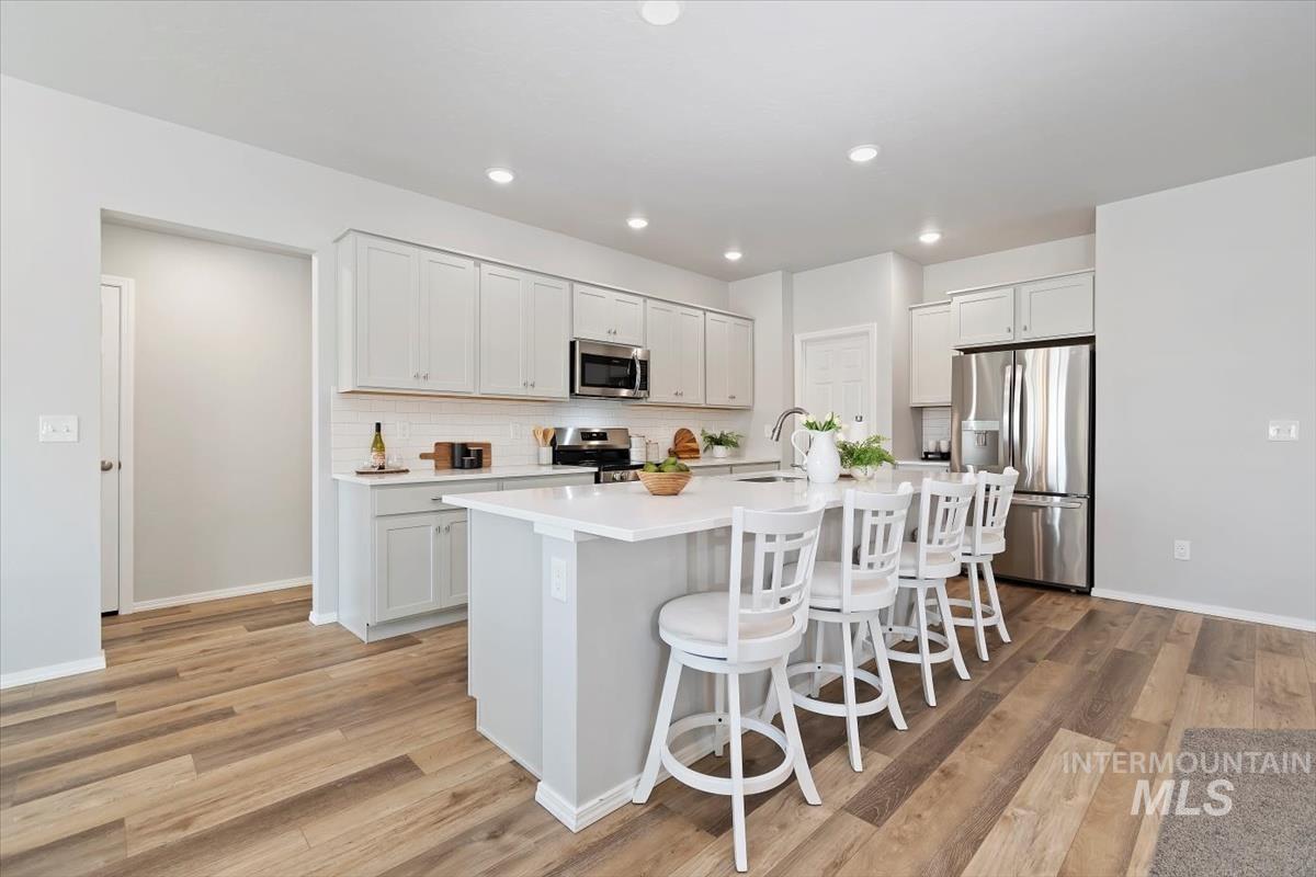 Kitchen featuring tasteful backsplash, appliances with stainless steel finishes, a breakfast bar area, a kitchen island with sink, and light wood-type flooring