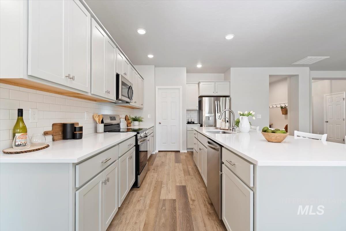 Kitchen featuring stainless steel appliances, light wood finished floors, an island with sink, white cabinetry, and recessed lighting