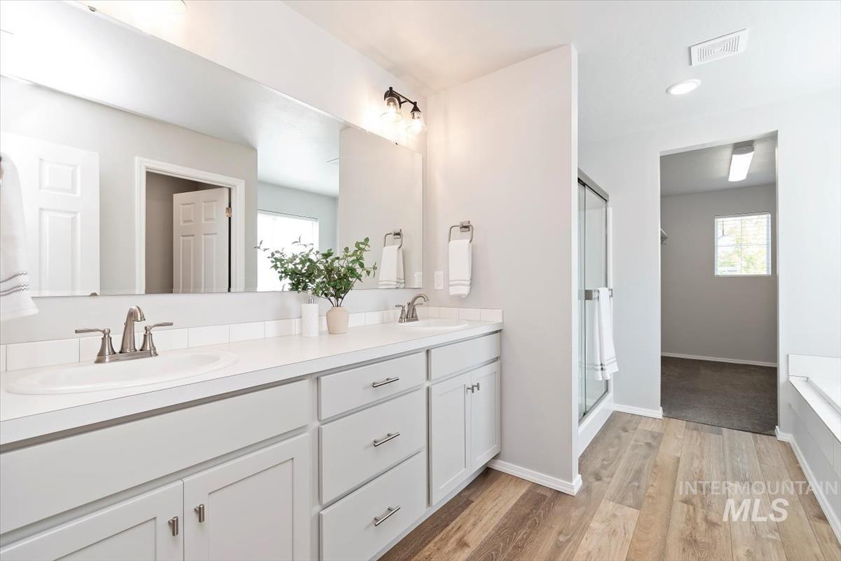 Bathroom featuring double vanity, light wood finished floors, a stall shower, plenty of natural light, and recessed lighting