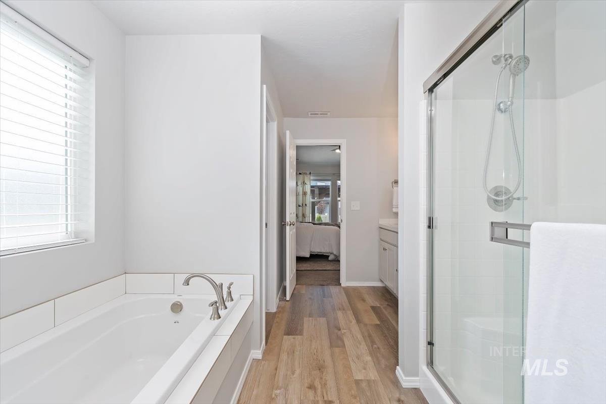 Full bathroom with light wood finished floors, a shower stall, ensuite bath, a garden tub, and vanity