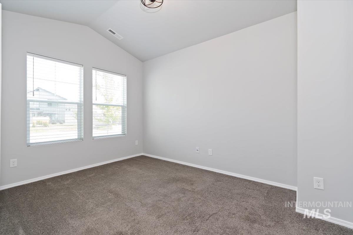 Spare room featuring vaulted ceiling and dark carpet