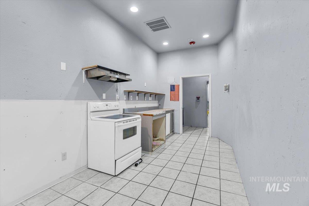 Kitchen featuring white range with electric stovetop, light tile patterned floors, light countertops, a textured wall, and open shelves
