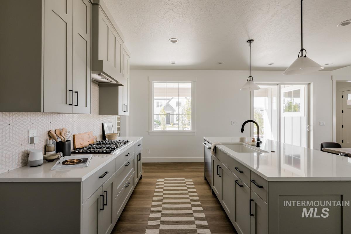 Kitchen featuring gray cabinets, backsplash, healthy amount of natural light, decorative light fixtures, and a textured ceiling