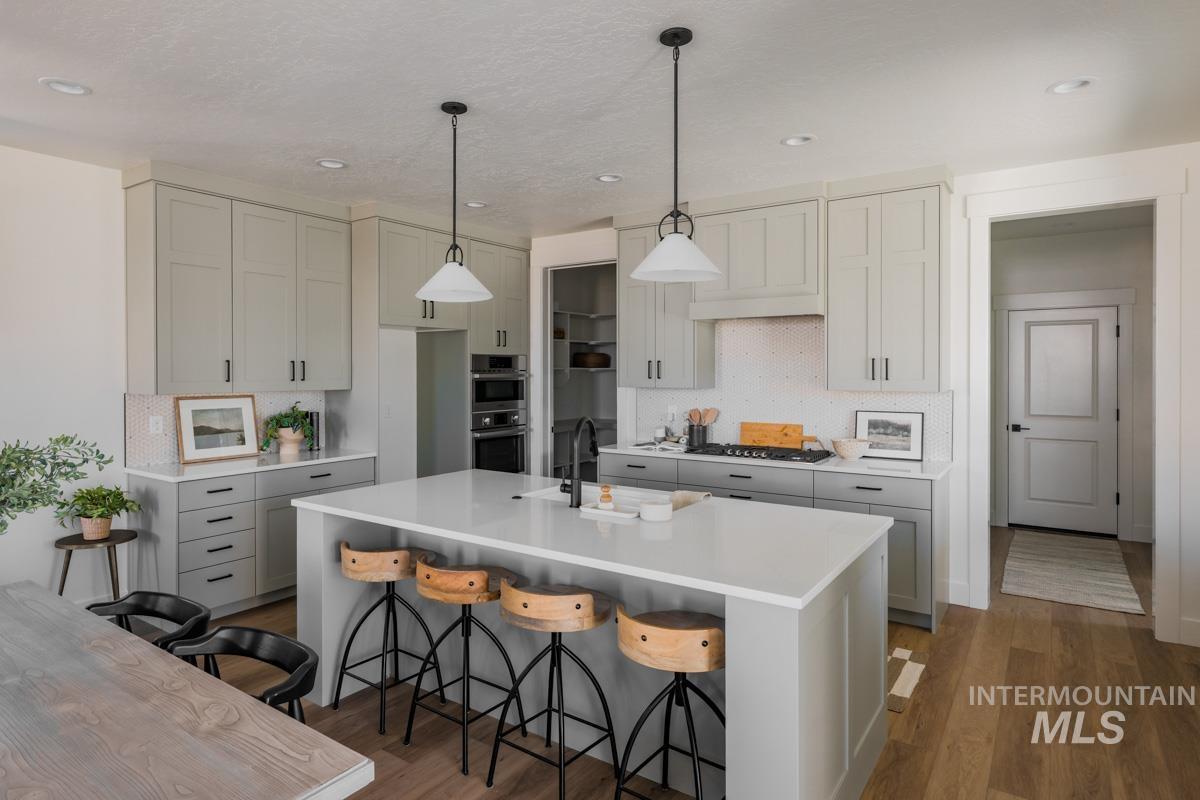 Kitchen with a breakfast bar area, decorative light fixtures, gray cabinets, dark wood-type flooring, and tasteful backsplash