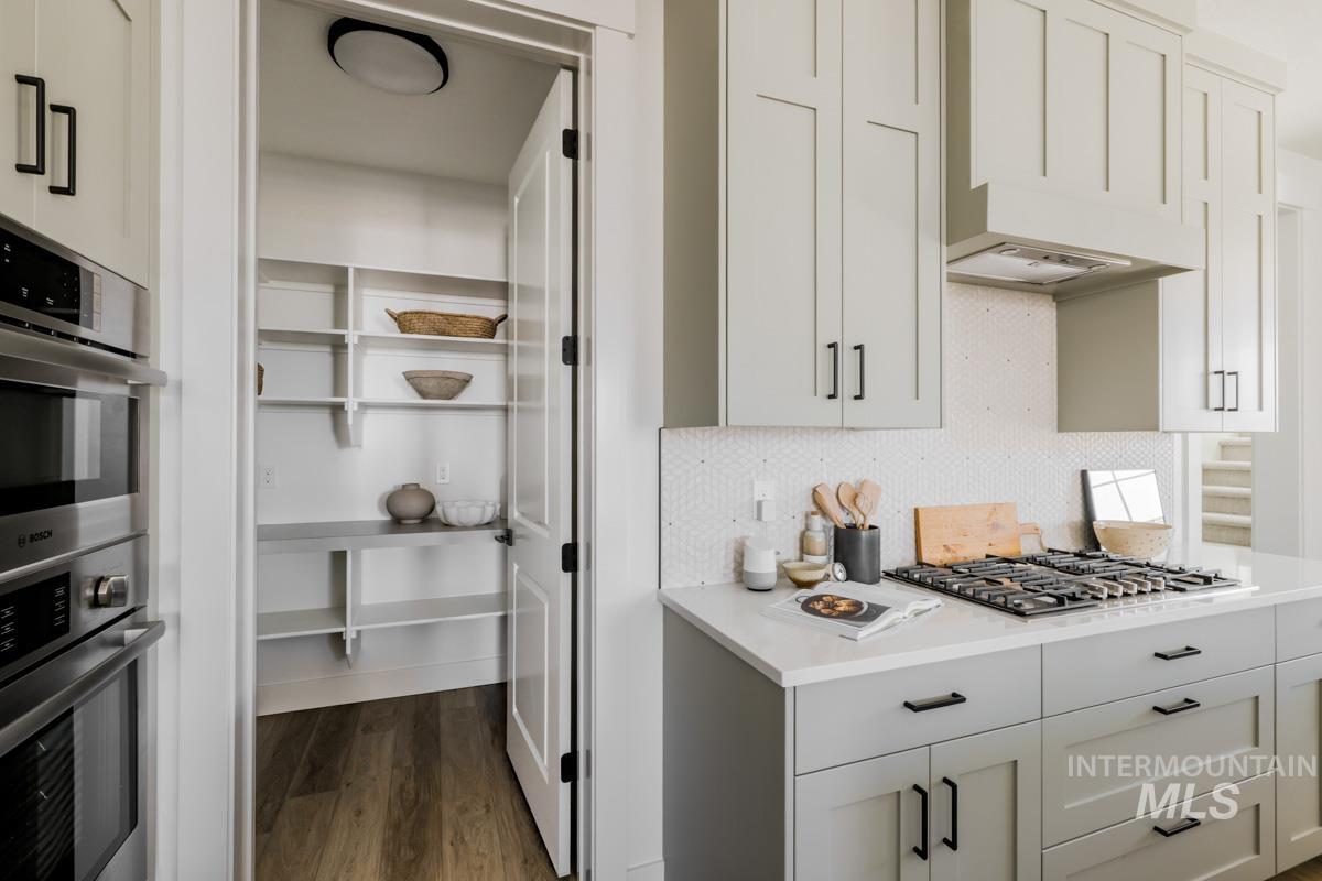 Kitchen featuring dark wood-type flooring, stainless steel appliances, decorative backsplash, and white cabinetry