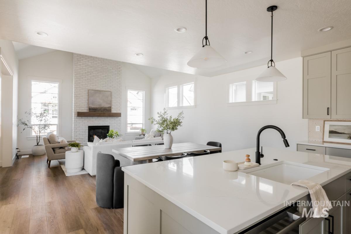 Kitchen with hanging light fixtures, vaulted ceiling, wood finished floors, open floor plan, and light stone countertops