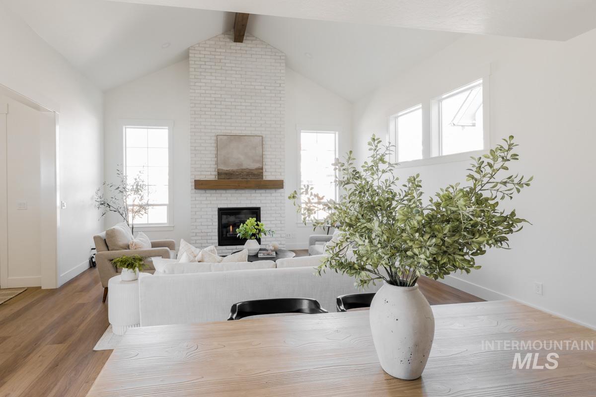 Living room featuring beam ceiling, wood finished floors, a brick fireplace, and high vaulted ceiling