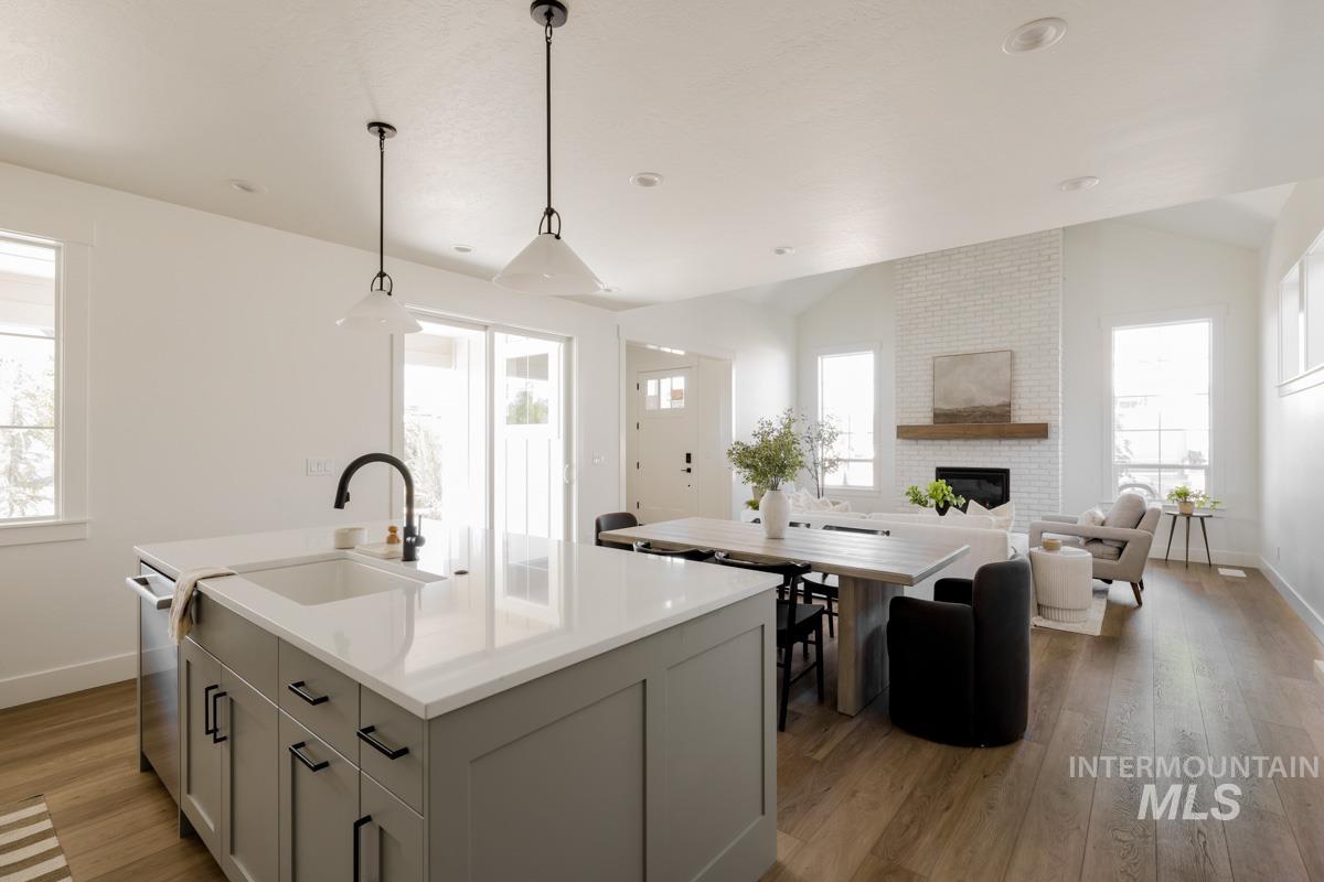 Kitchen featuring gray cabinets, open floor plan, hanging light fixtures, light wood-style flooring, and an island with sink