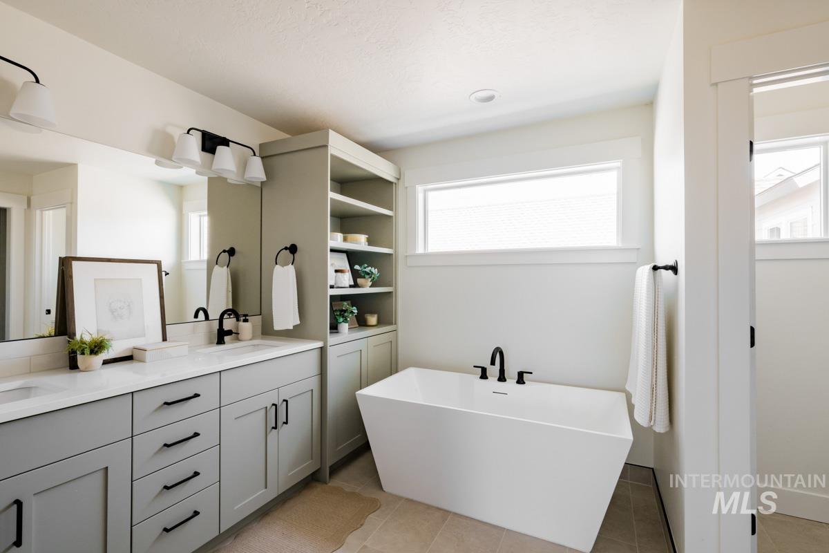 Full bath with double vanity, a soaking tub, light tile patterned floors, and healthy amount of natural light