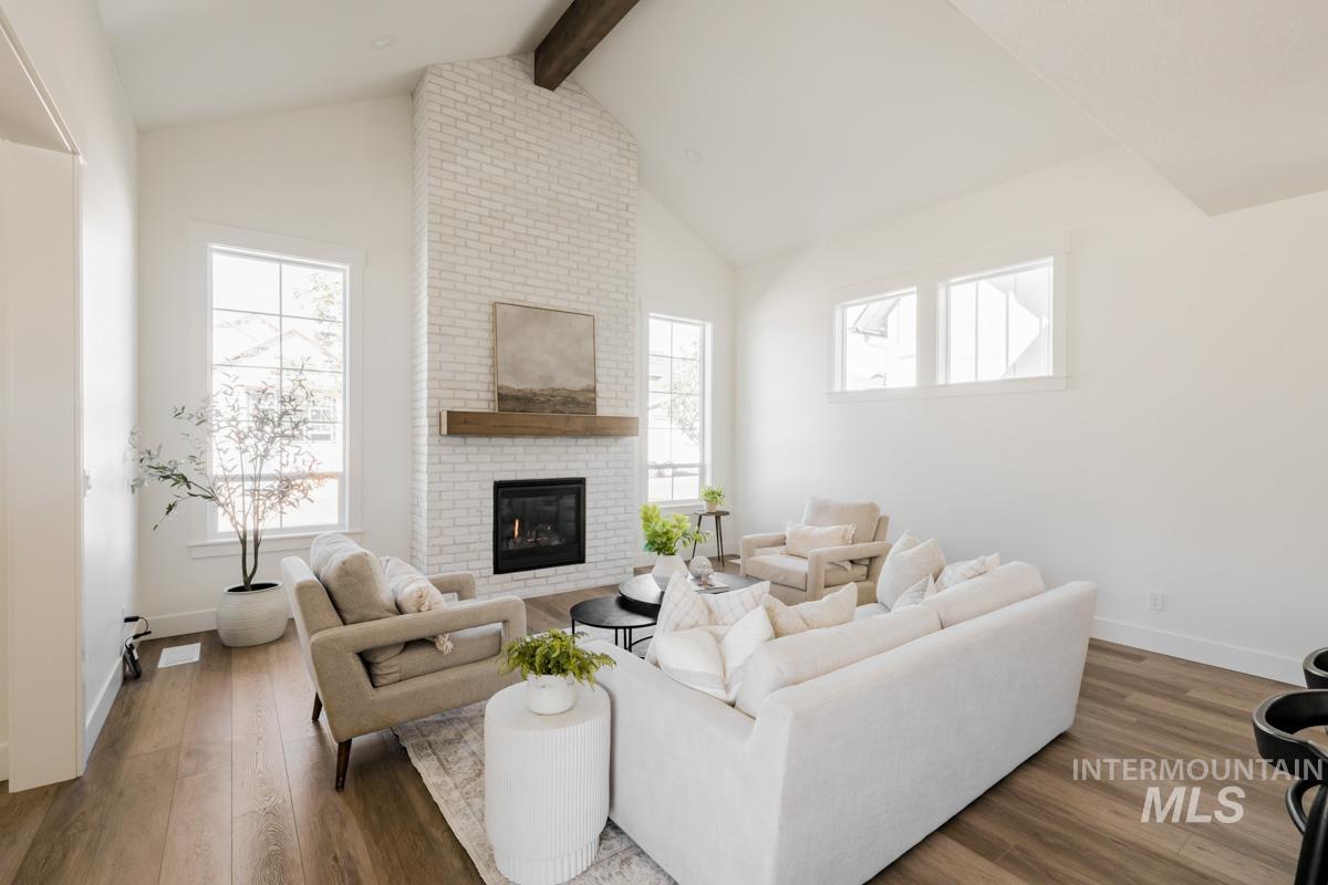 Living area featuring beam ceiling, wood finished floors, a brick fireplace, and high vaulted ceiling