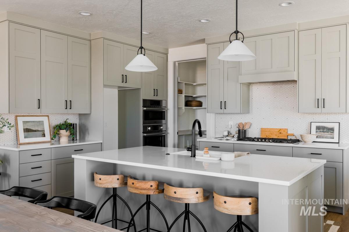 Kitchen with decorative backsplash, a breakfast bar, pendant lighting, gray cabinets, and a kitchen island with sink