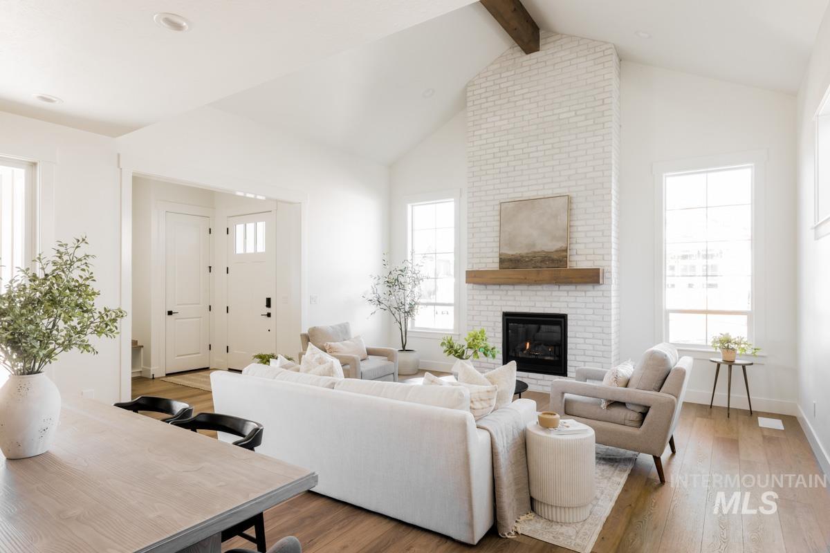 Living area featuring light wood-type flooring, beamed ceiling, high vaulted ceiling, and a brick fireplace
