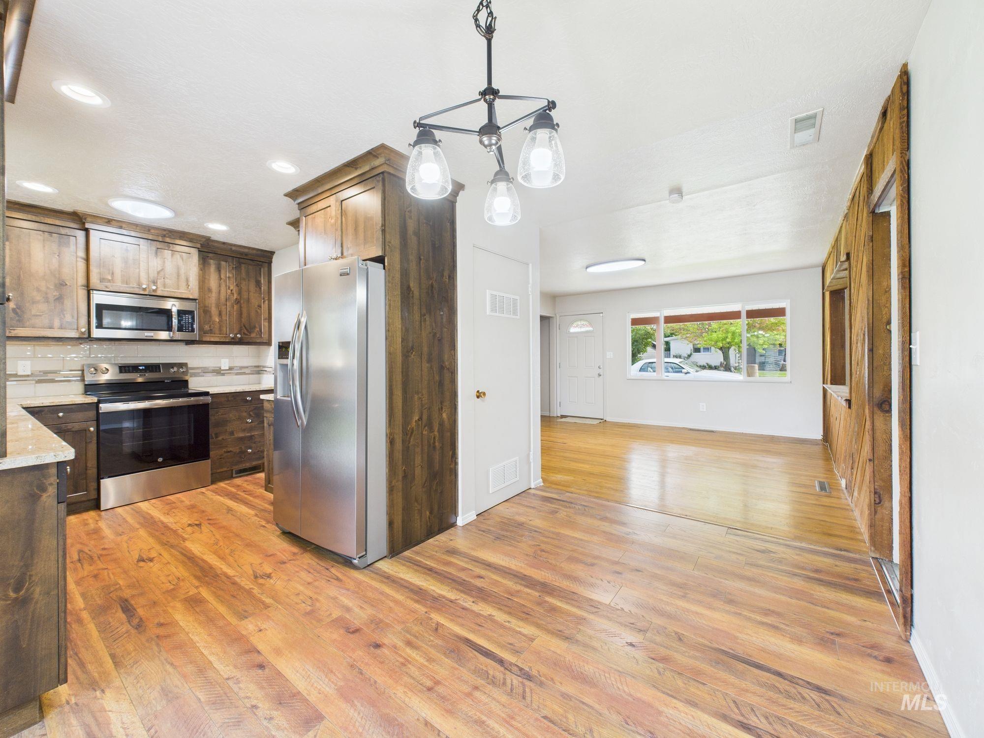 Kitchen with stainless steel appliances, decorative light fixtures, light wood finished floors, a chandelier, and backsplash