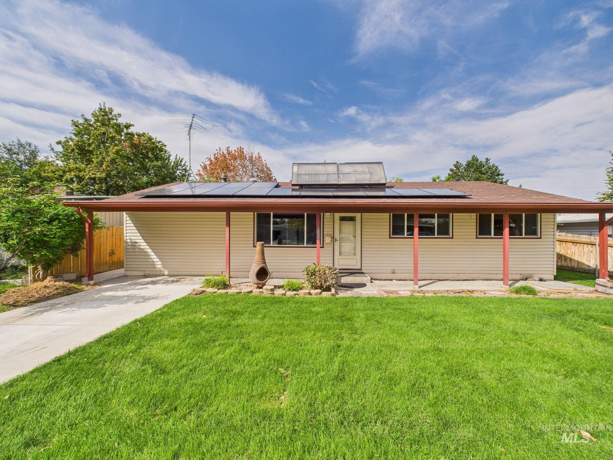 View of front facade featuring driveway, an attached carport, roof mounted solar panels, and a patio