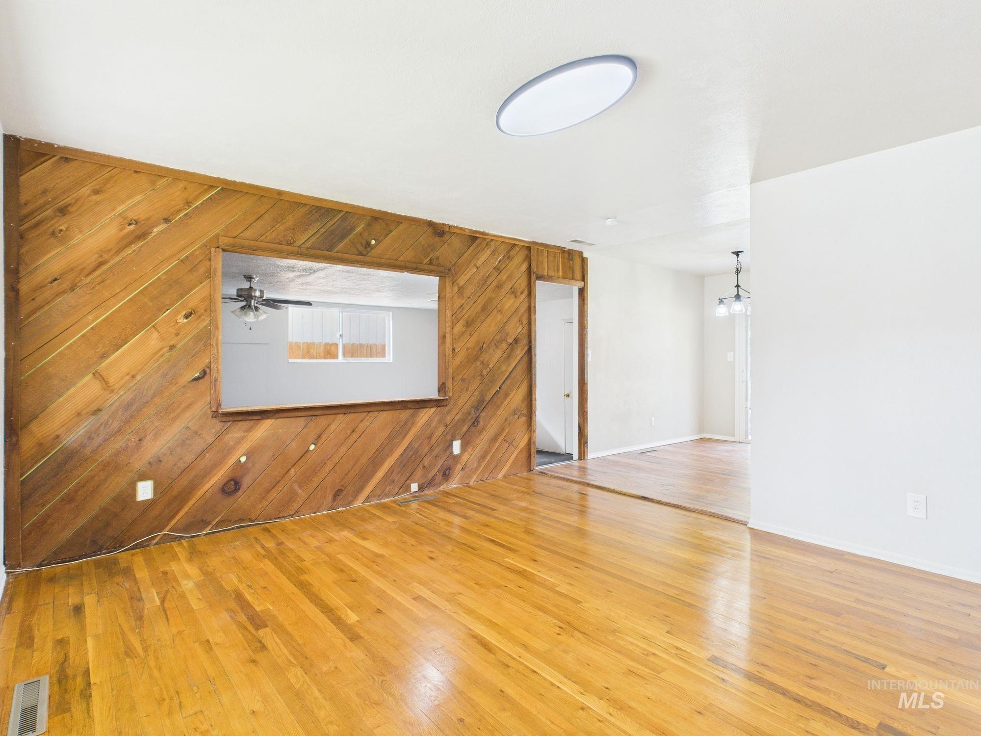 Unfurnished living room featuring wood walls, light wood-type flooring, and a chandelier