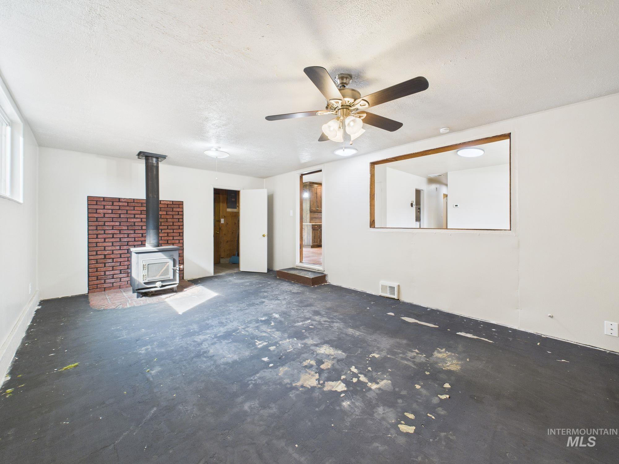Unfurnished living room with a wood stove, a textured ceiling, and ceiling fan
