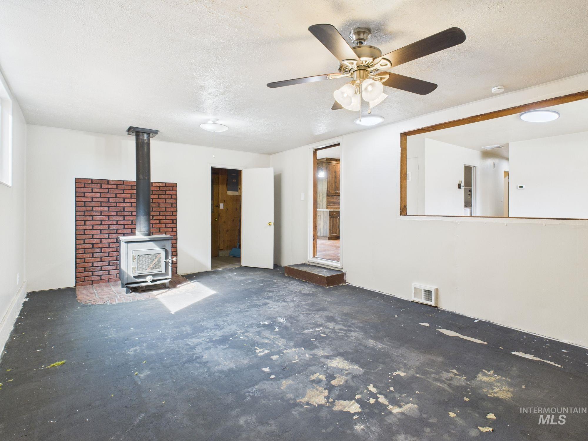 Unfurnished living room with a wood stove, a textured ceiling, ceiling fan, and concrete floors
