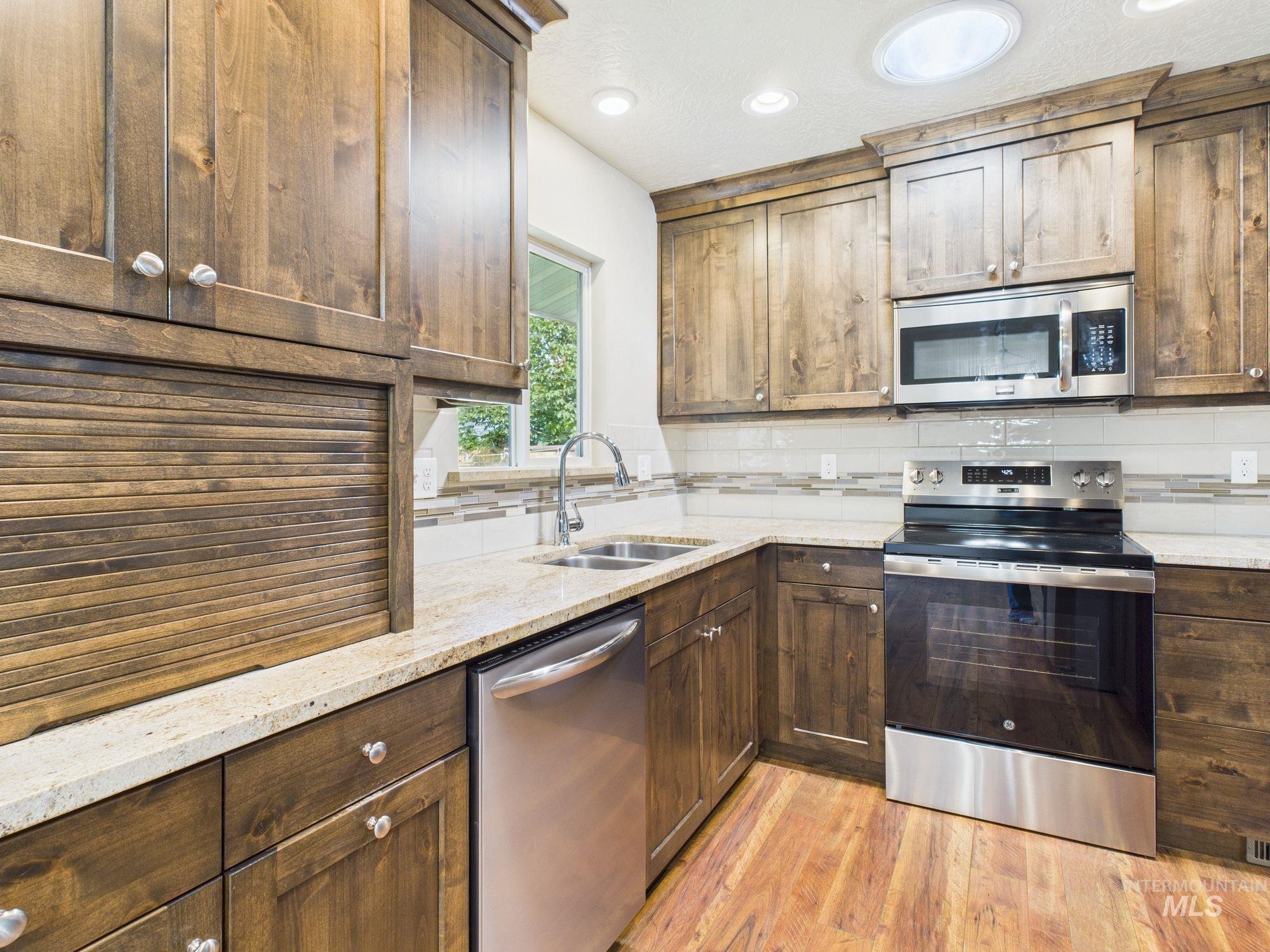 Kitchen with appliances with stainless steel finishes, backsplash, light stone countertops, light wood-style floors, and recessed lighting
