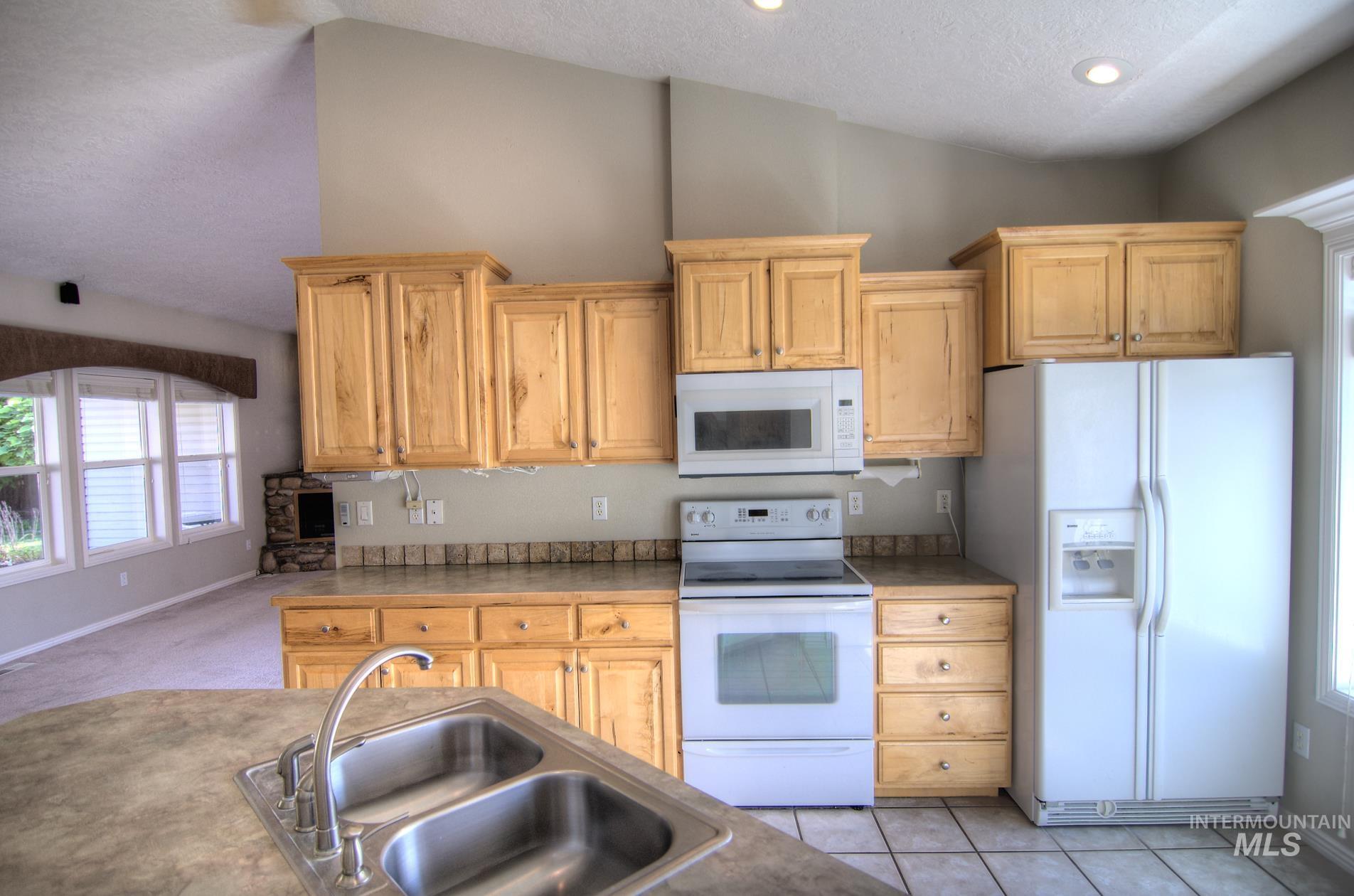 Kitchen with plenty of natural light, white appliances, a textured ceiling, light tile patterned floors, and light carpet