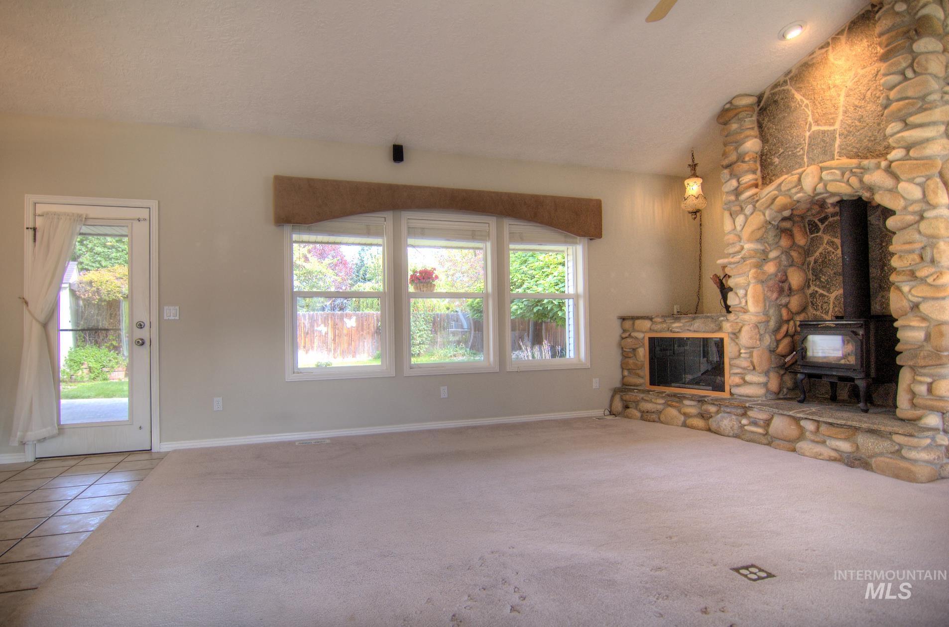 Unfurnished living room featuring tile patterned floors, a wood stove, vaulted ceiling, and carpet floors
