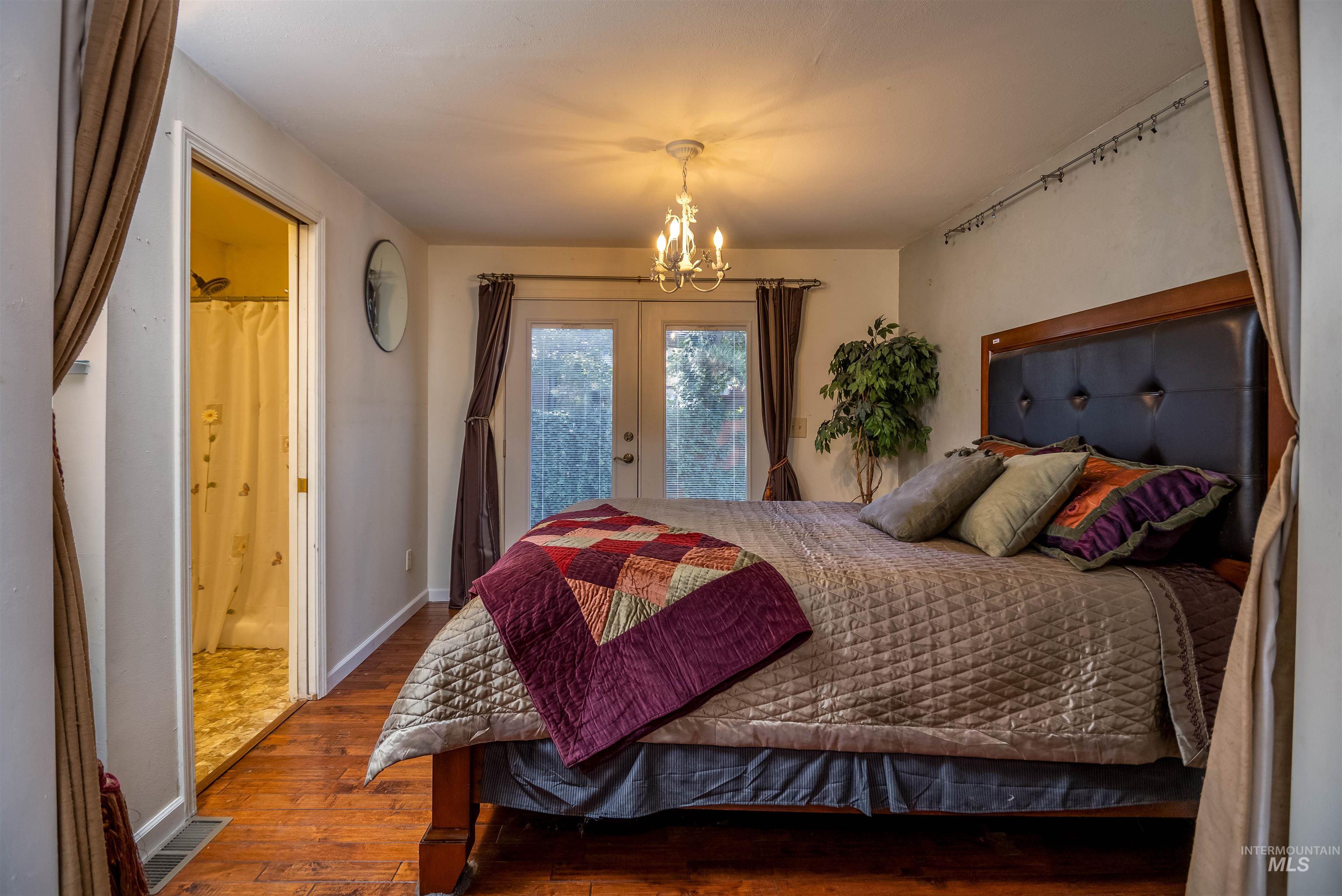 Bedroom featuring wood-type flooring, access to exterior, french doors, a chandelier, and ensuite bathroom