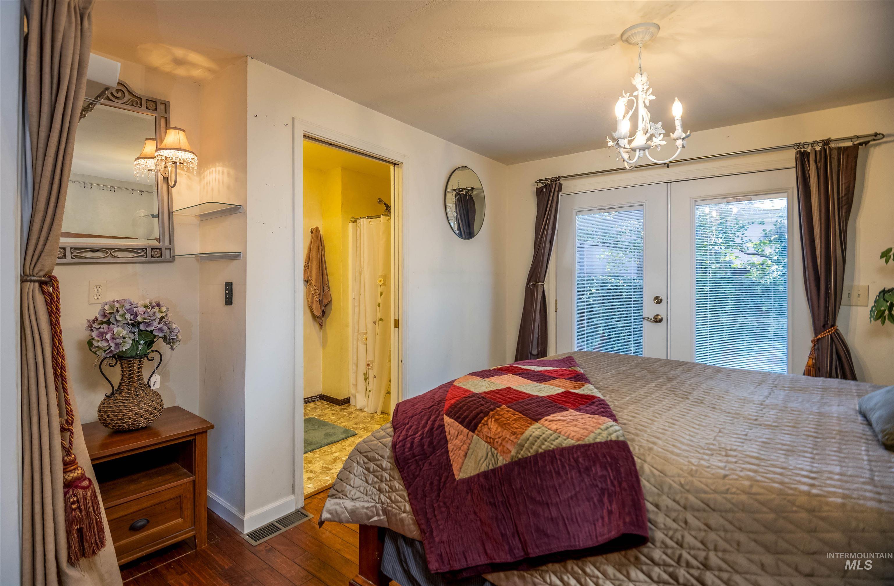 Bedroom featuring a chandelier, hardwood / wood-style flooring, french doors, access to exterior, and ensuite bath