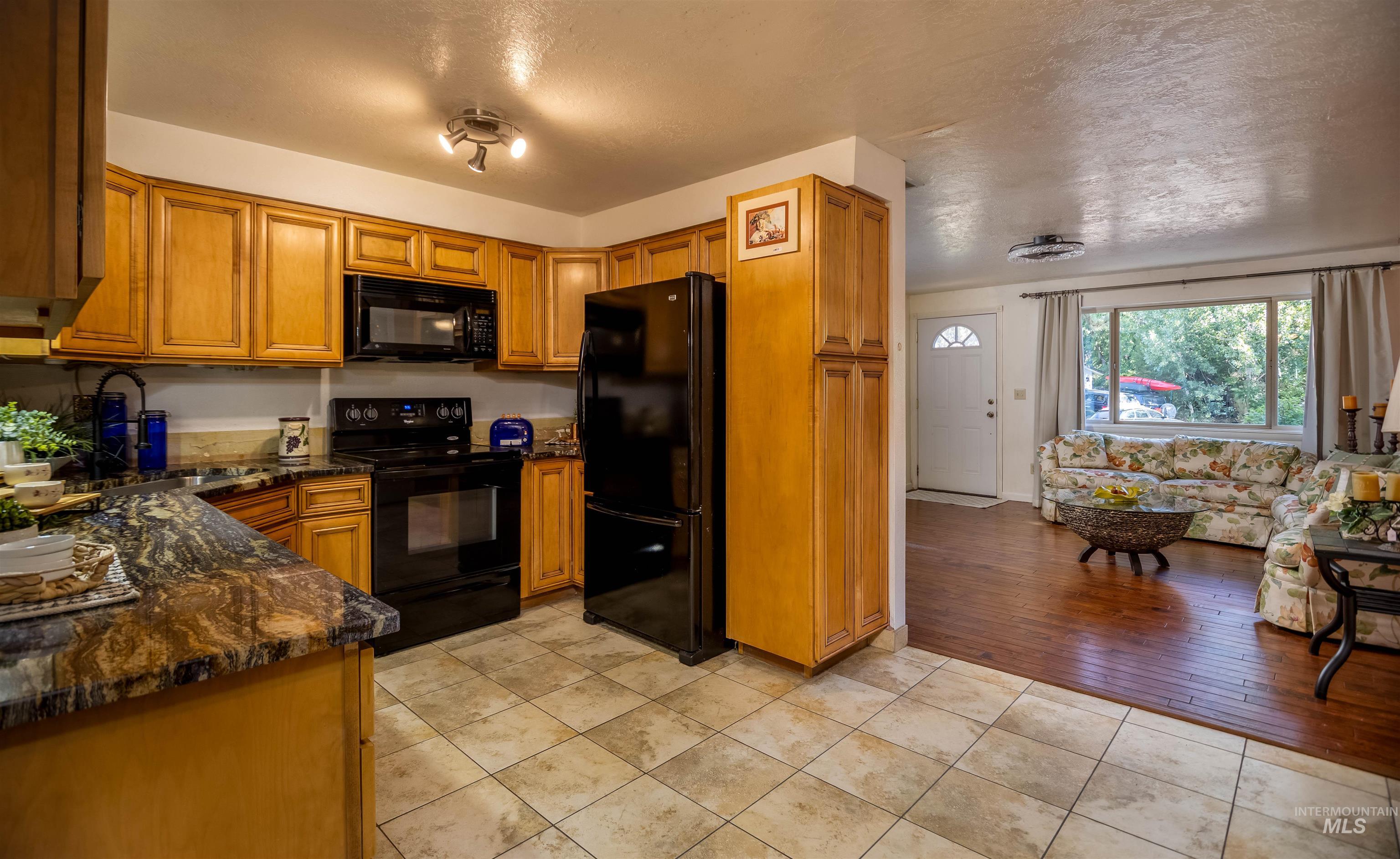Kitchen featuring brown cabinets, black appliances, dark stone counters, light tile patterned floors, and a textured ceiling