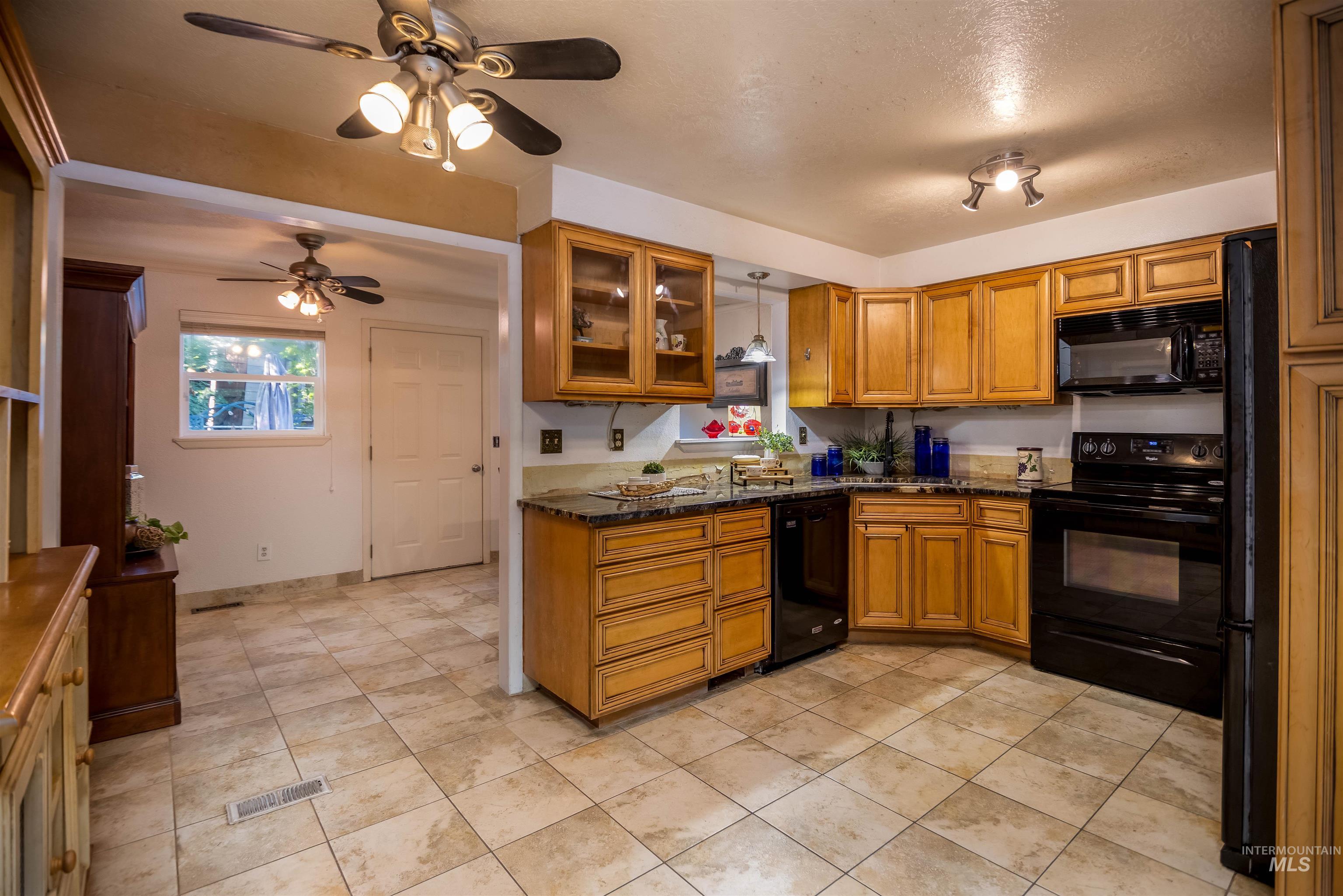 Kitchen featuring brown cabinets, glass insert cabinets, black appliances, and ceiling fan