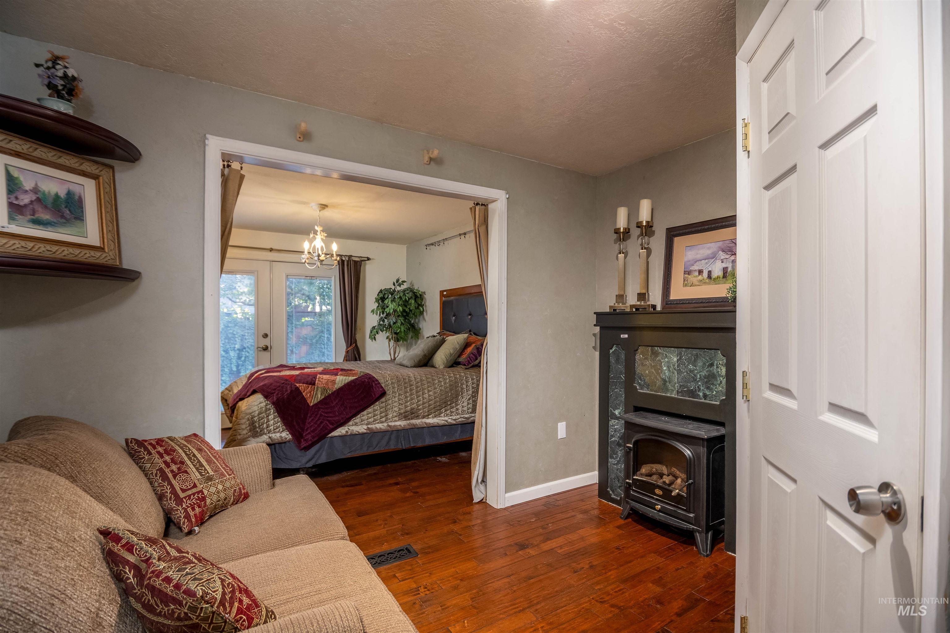 Bedroom featuring dark wood finished floors, a chandelier, a wood stove, and a textured ceiling