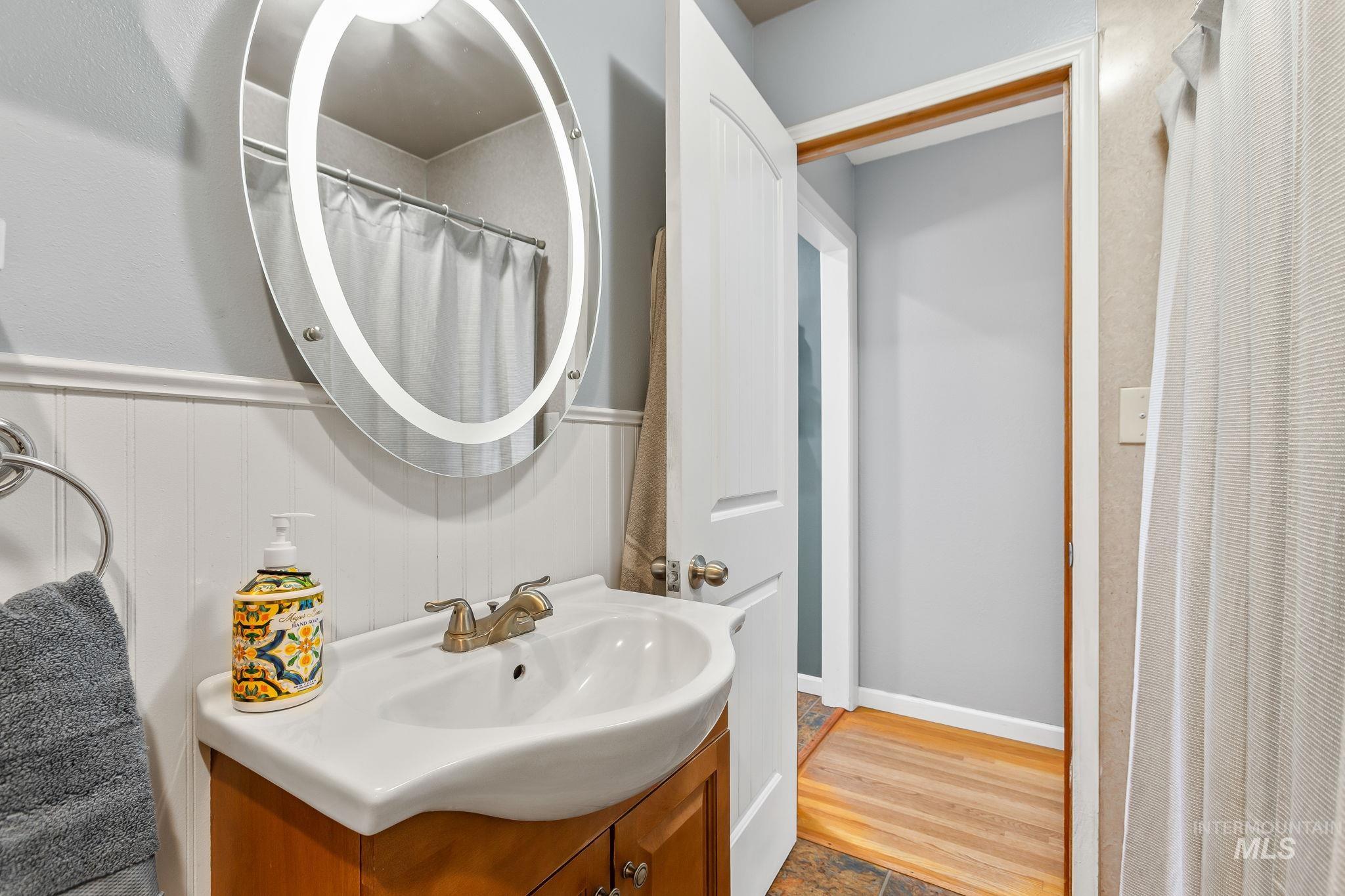 Full bathroom with vanity, a wainscoted wall, and wood finished floors
