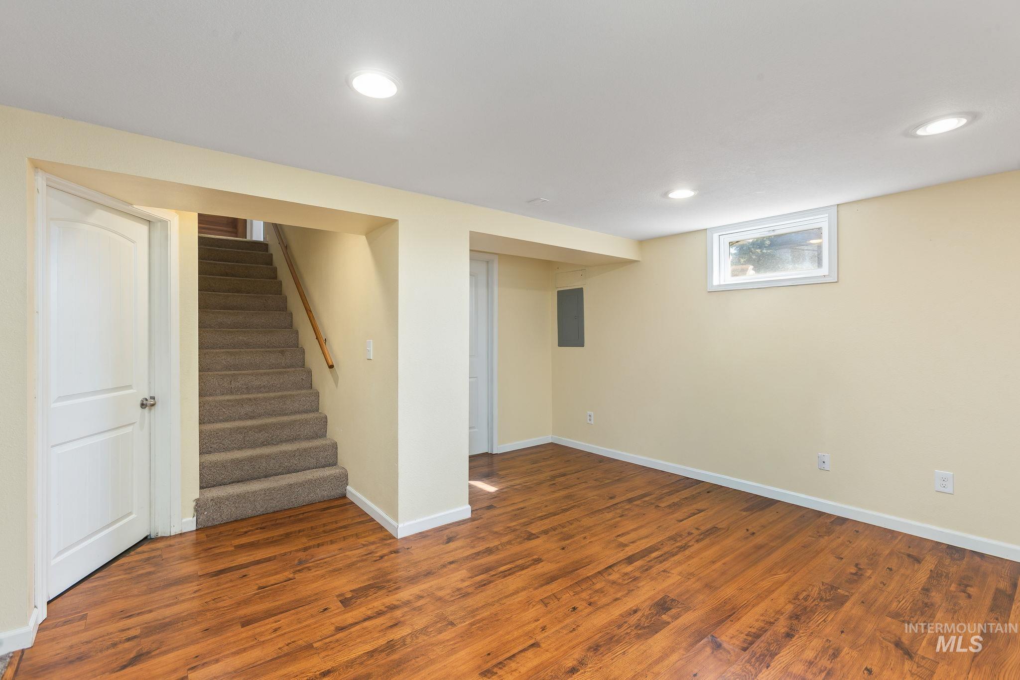 Basement with dark wood-style flooring, stairway, recessed lighting, and electric panel