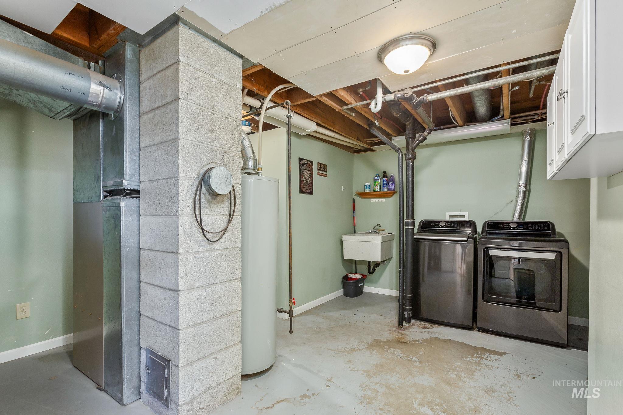 Laundry area featuring heating unit, water heater, washer and clothes dryer, and cabinet space