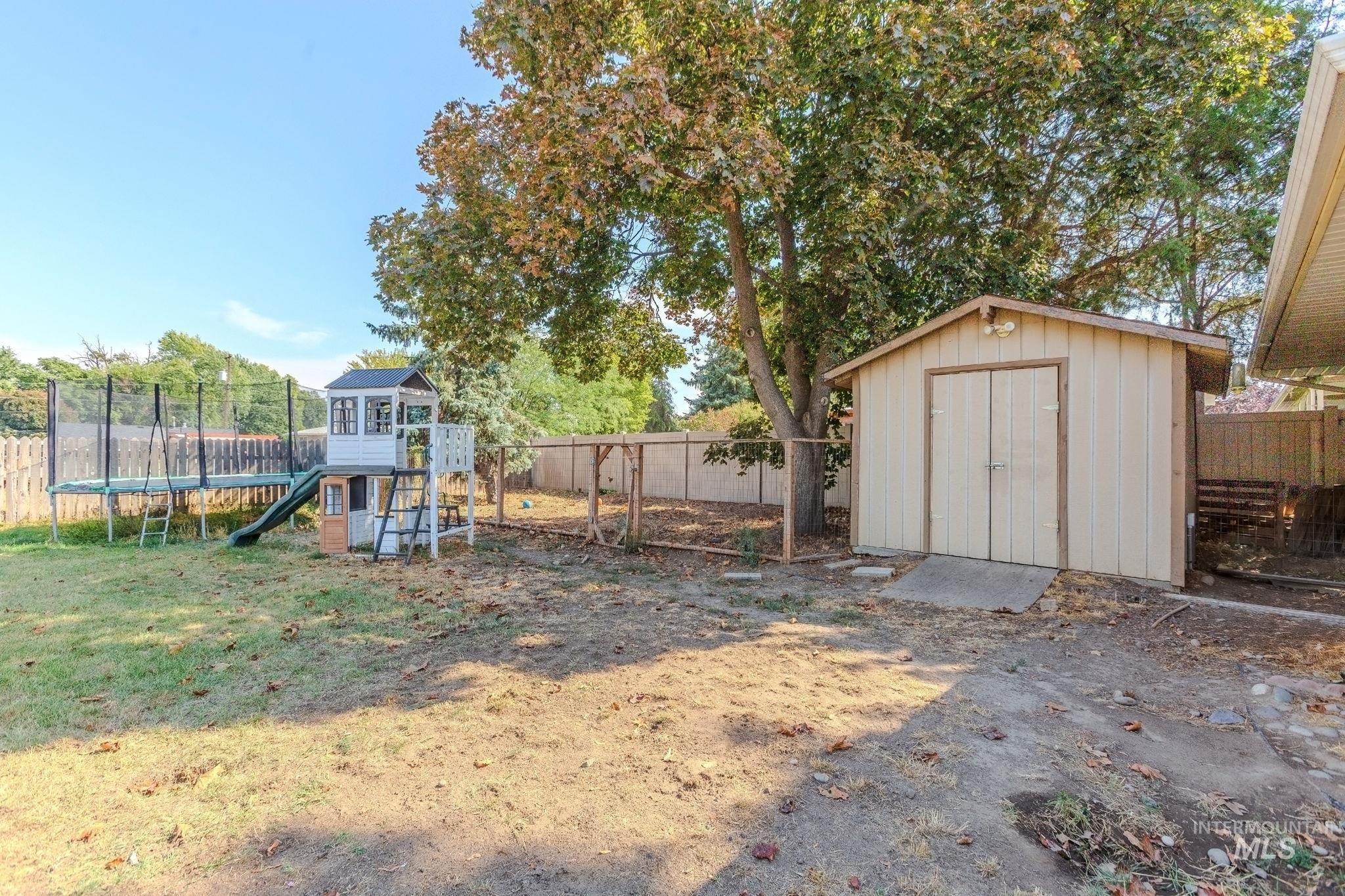 Fenced backyard featuring a trampoline and a storage shed