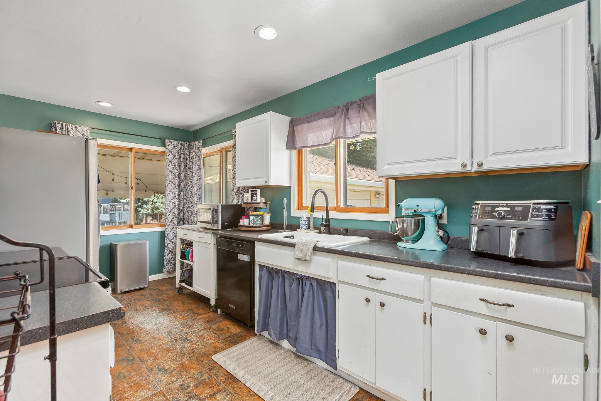 Kitchen with dark countertops, white cabinets, black appliances, and recessed lighting
