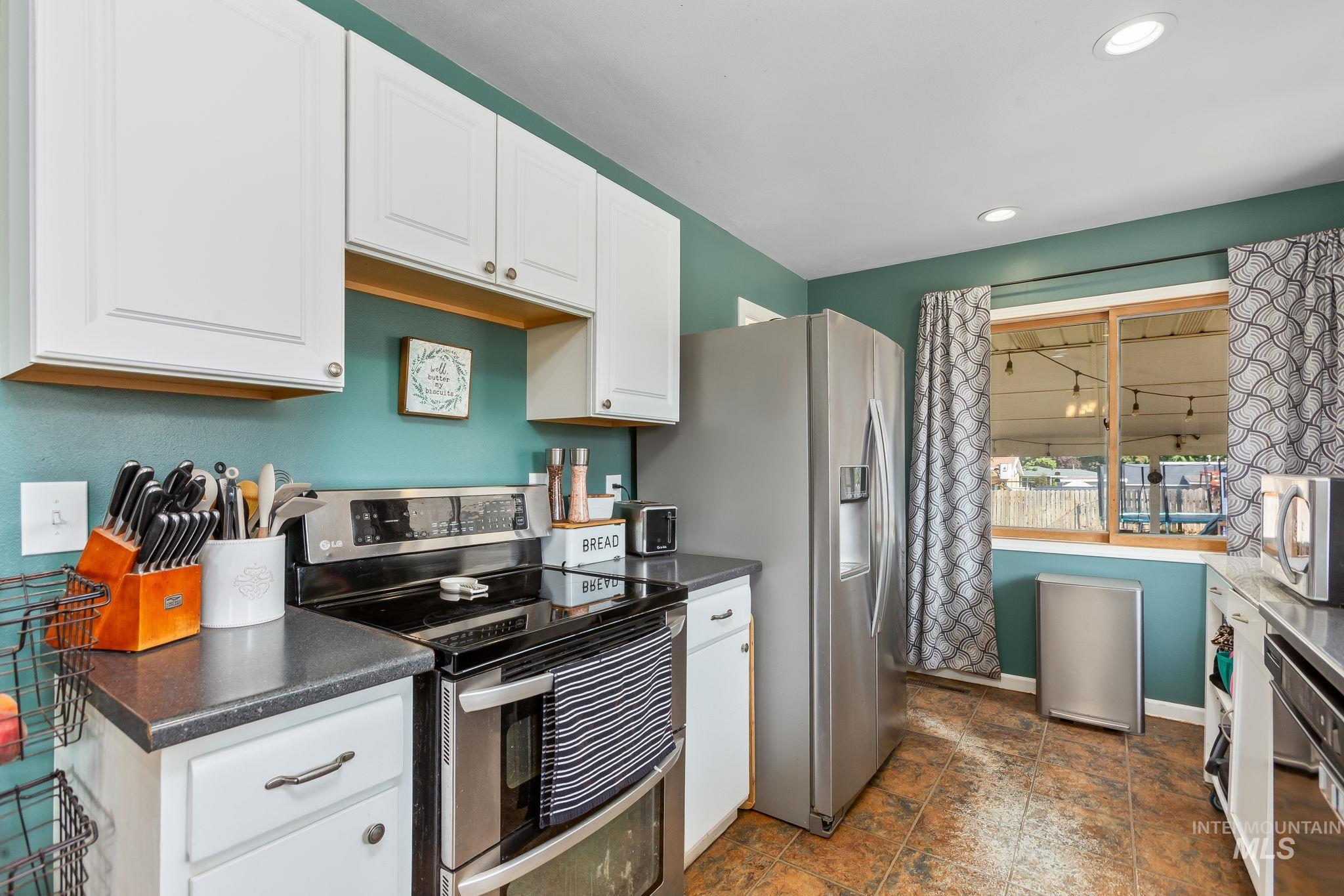 Kitchen featuring appliances with stainless steel finishes, dark countertops, white cabinetry, recessed lighting, and dark stone finish floors