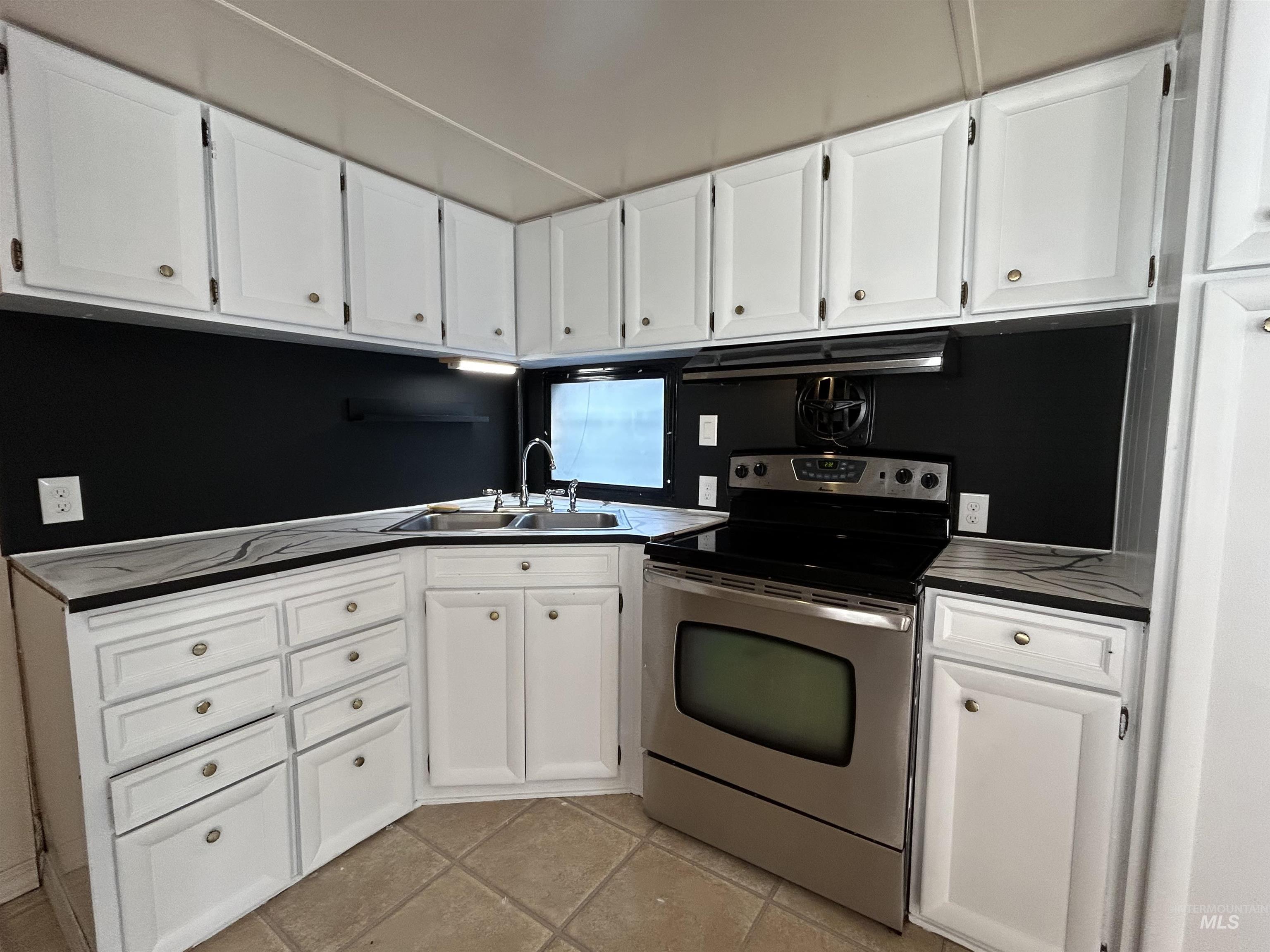 Kitchen featuring stainless steel range with electric stovetop, white cabinetry, dark countertops, and ventilation hood