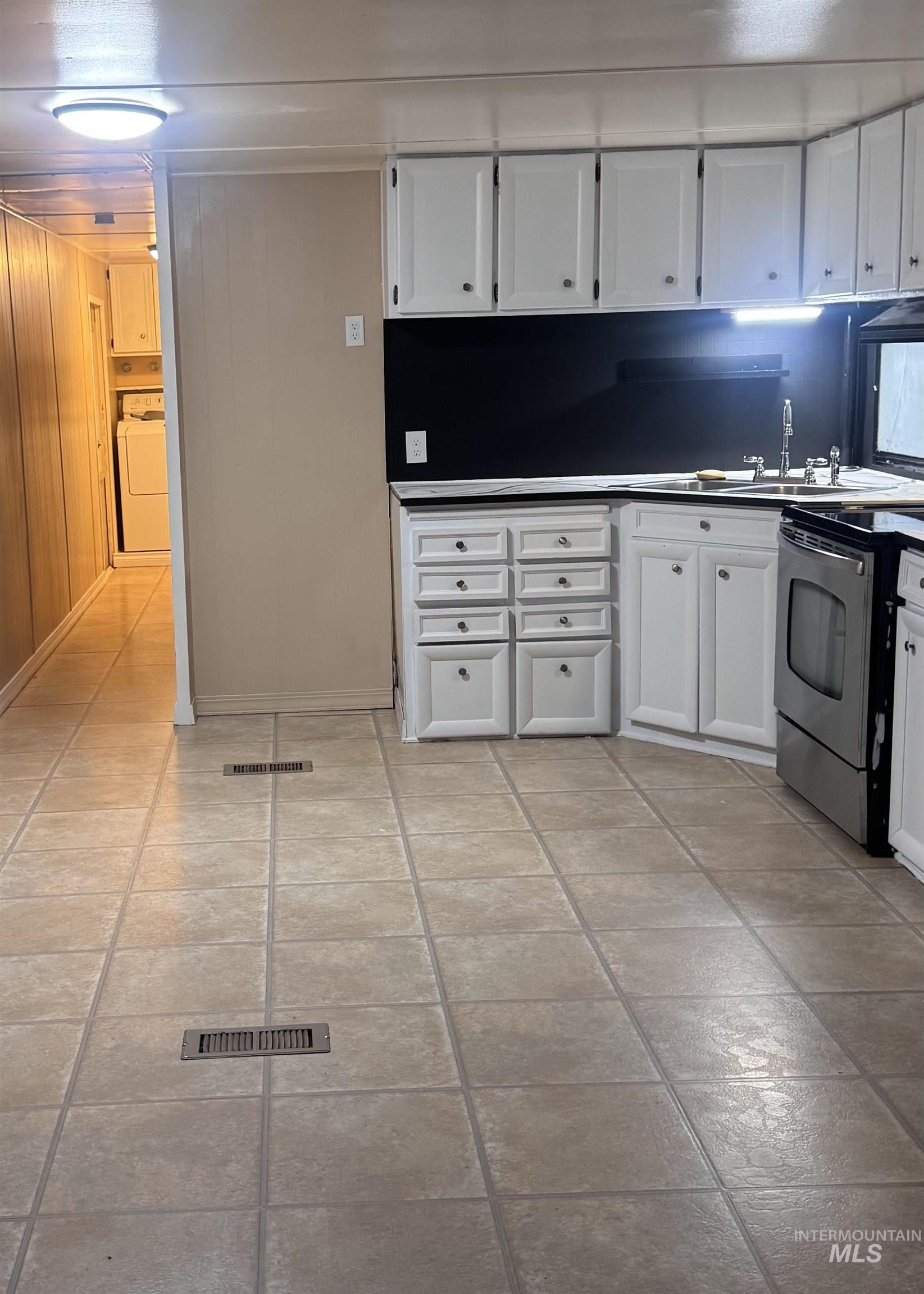 Kitchen featuring white cabinets, stainless steel range with electric cooktop, washer / clothes dryer, light tile patterned floors, and dark countertops