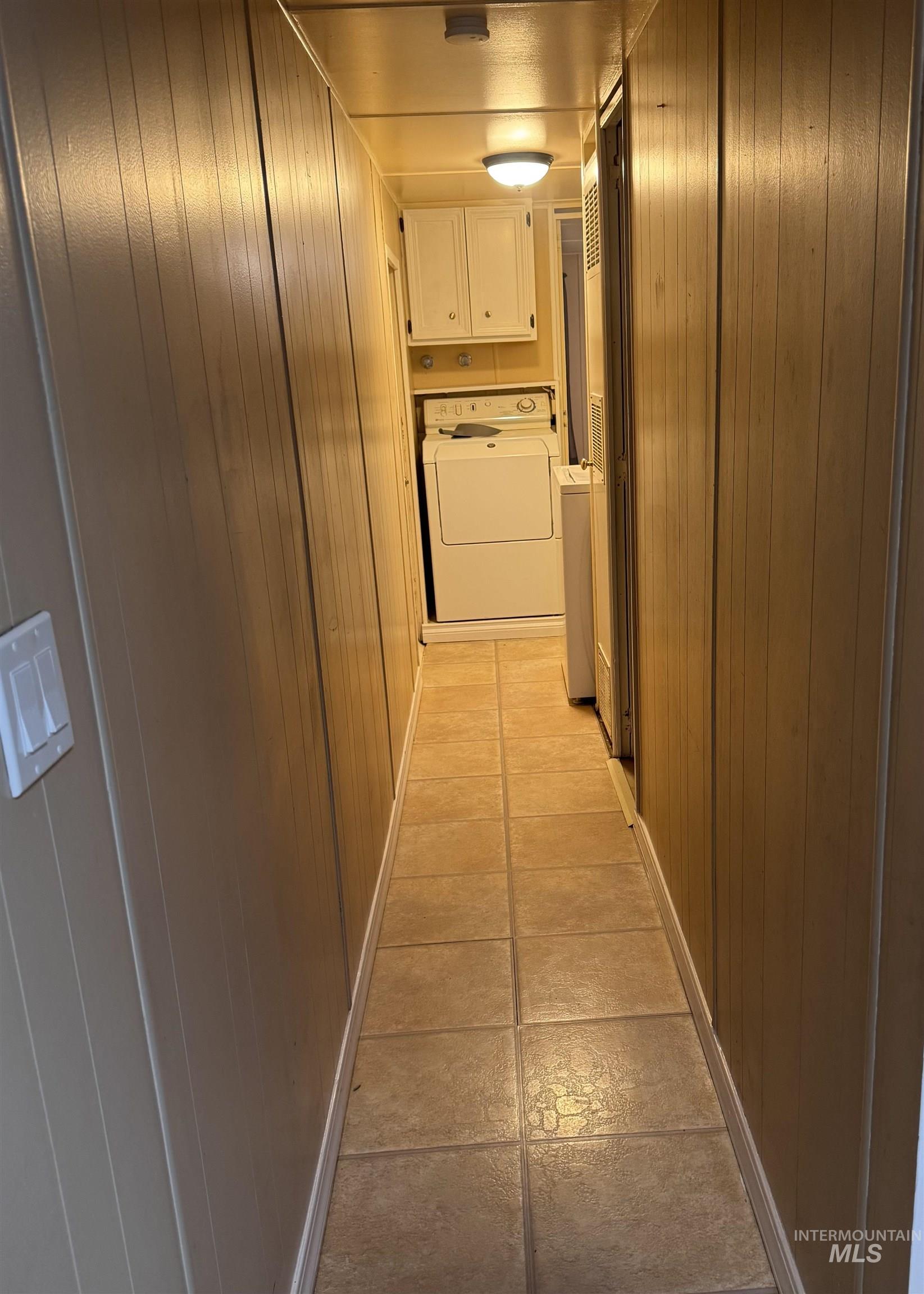 Corridor featuring wooden walls, separate washer and dryer, and light tile patterned flooring