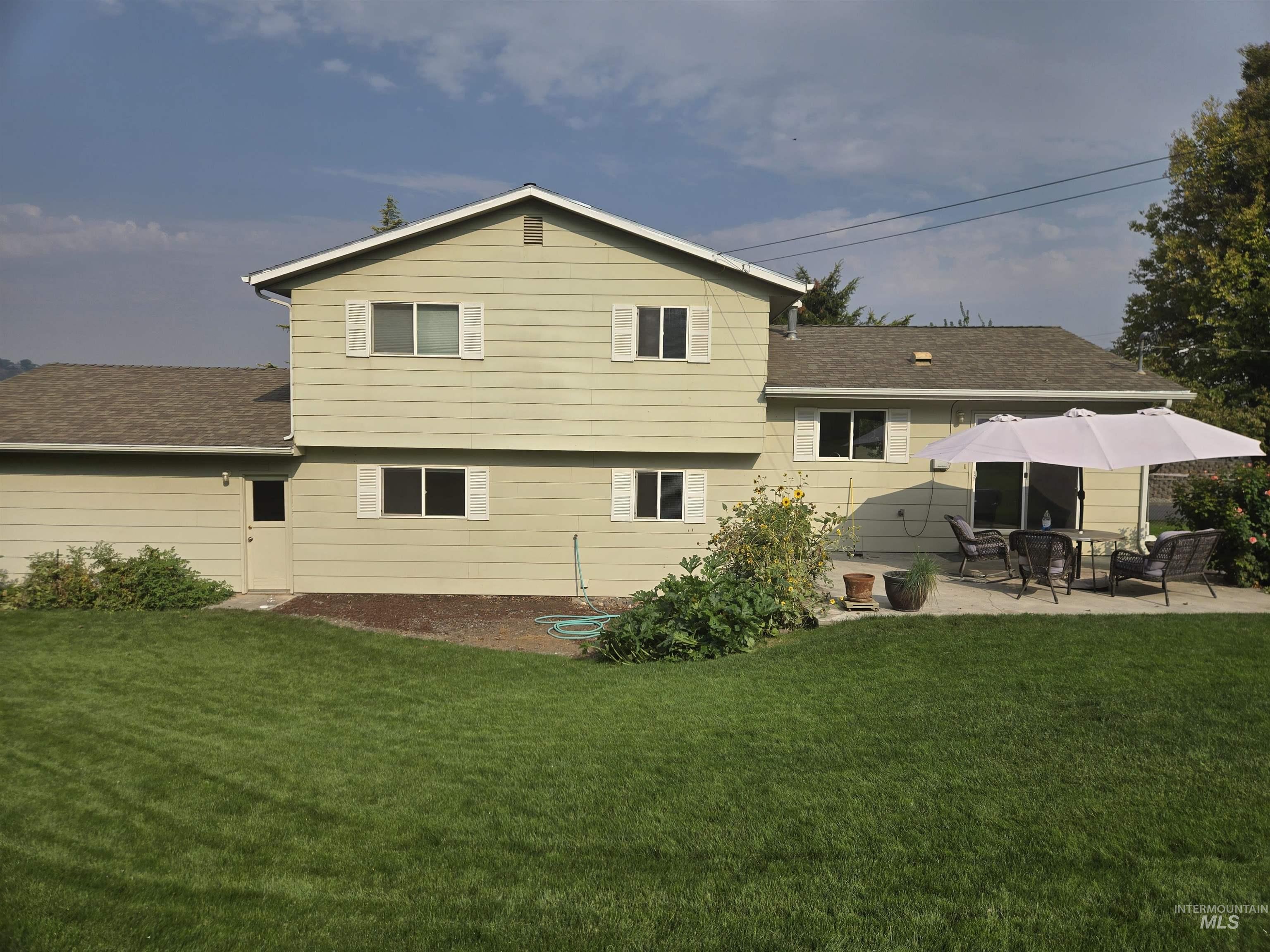 Rear view of property with a yard, a shingled roof, and a patio
