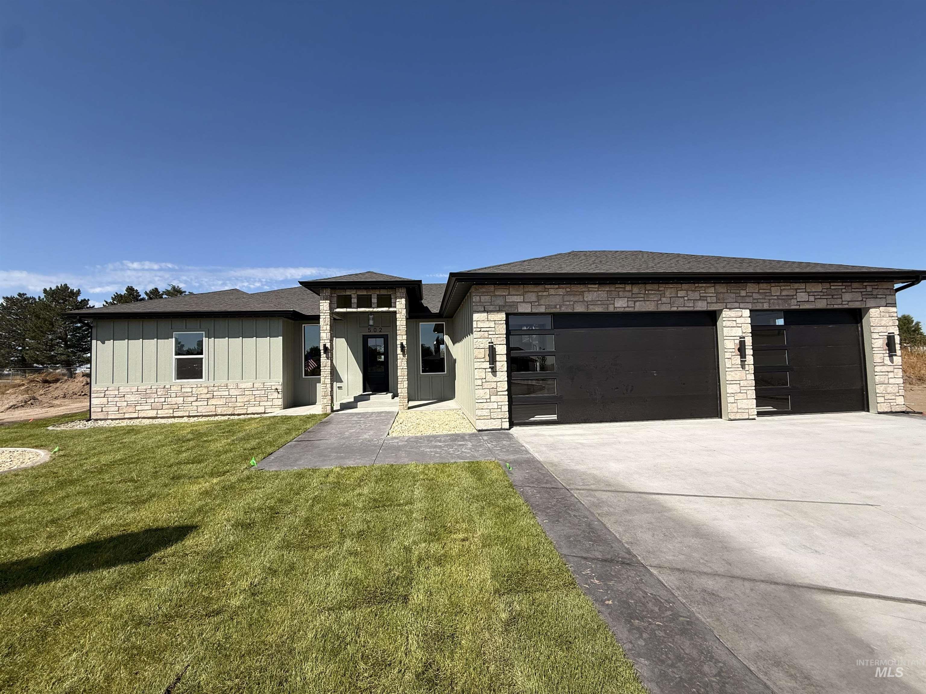 Prairie-style house with stone siding, board and batten siding, driveway, a front yard, and an attached garage