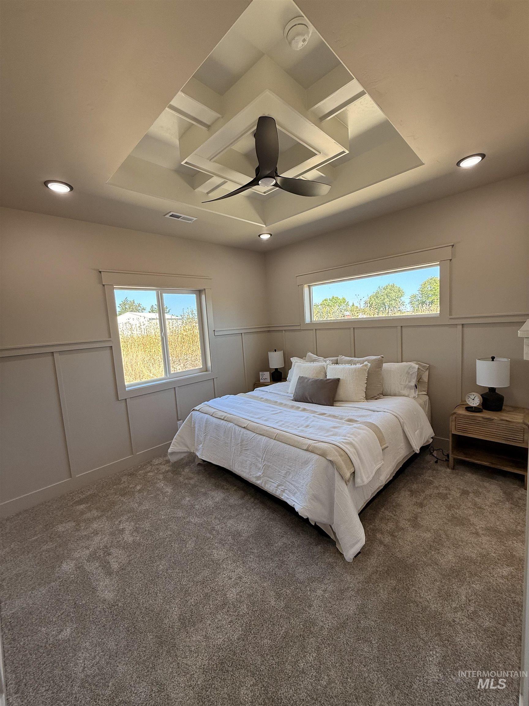 Carpeted bedroom with a tray ceiling, a decorative wall, wainscoting, a ceiling fan, and recessed lighting
